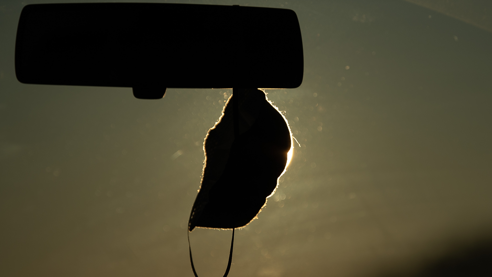 Eine FFP2-Maske hängt vor der aufgehenden Sonne in einem Auto.  | dpa