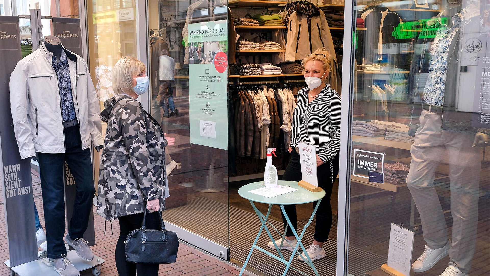 Eine Modehändlerin unterhält sich am Eingang ihres Geschäftes mit einer Kundin | picture alliance / Rupert Oberh