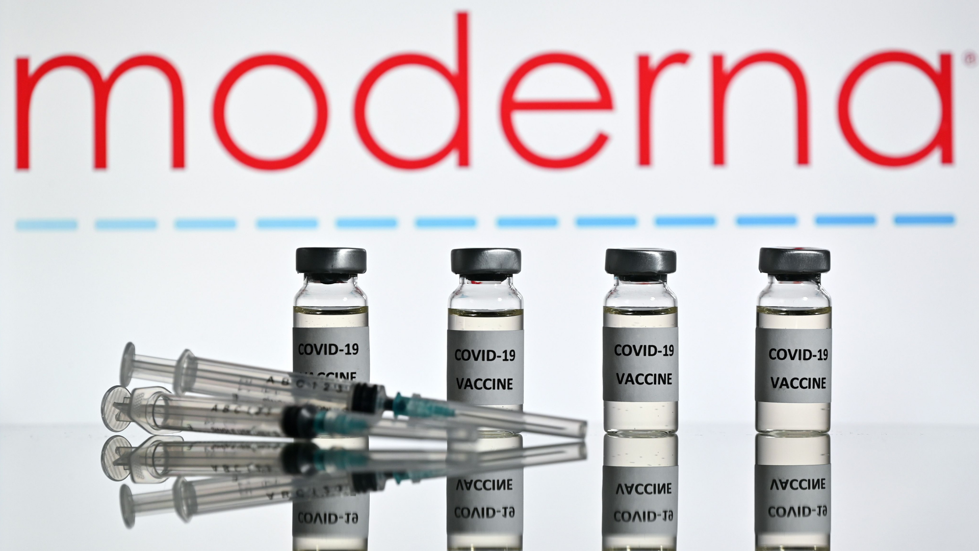 Spritzen und Ampullen eines Corona-Impfstoffes vor dem Logo des US-Herstellers Moderna | AFP