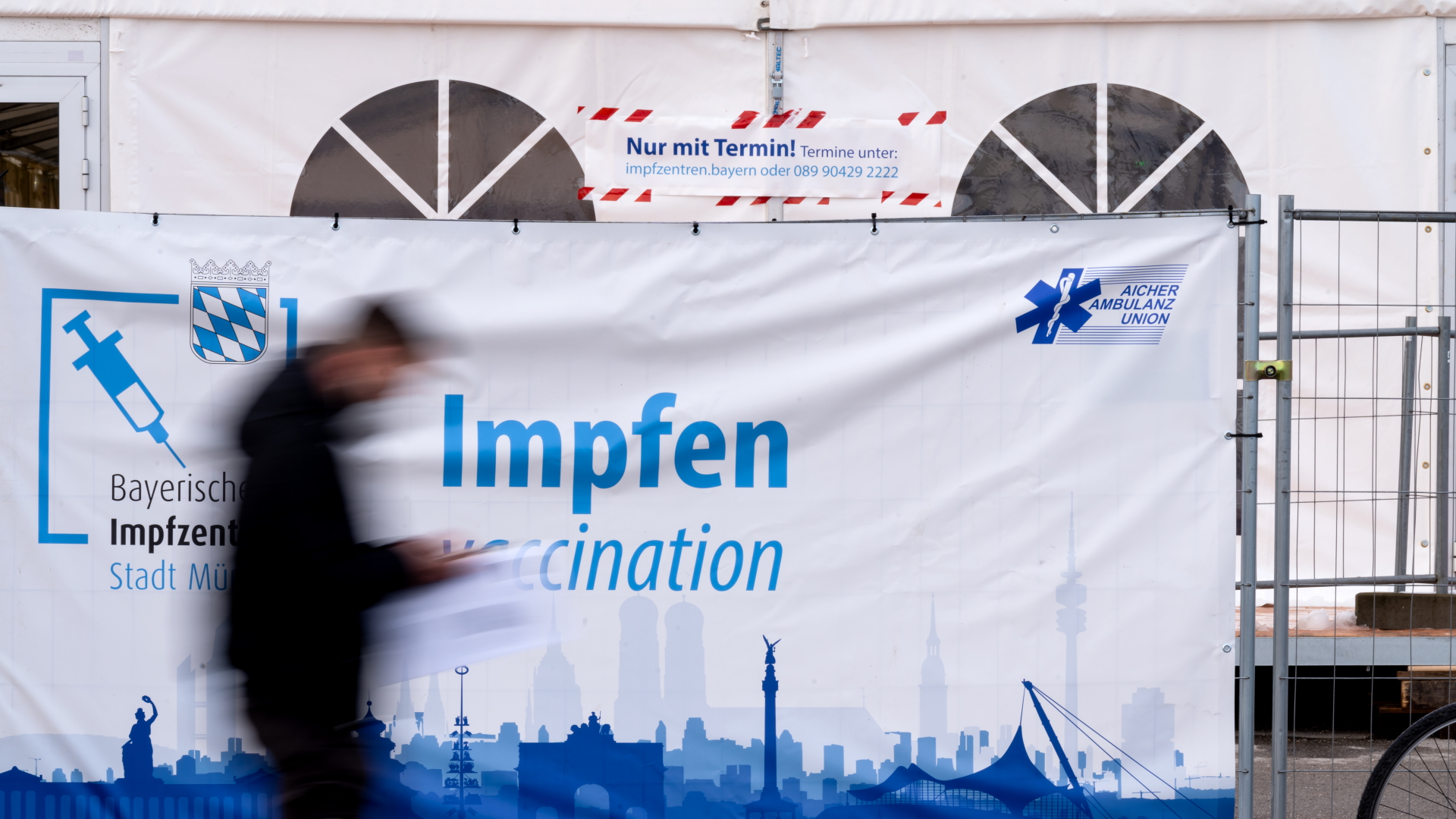 Ein Mann geht auf der Münchner Theresienwiese an einem Plakat mit der Aufschrift "Impfen" vorbei. | dpa