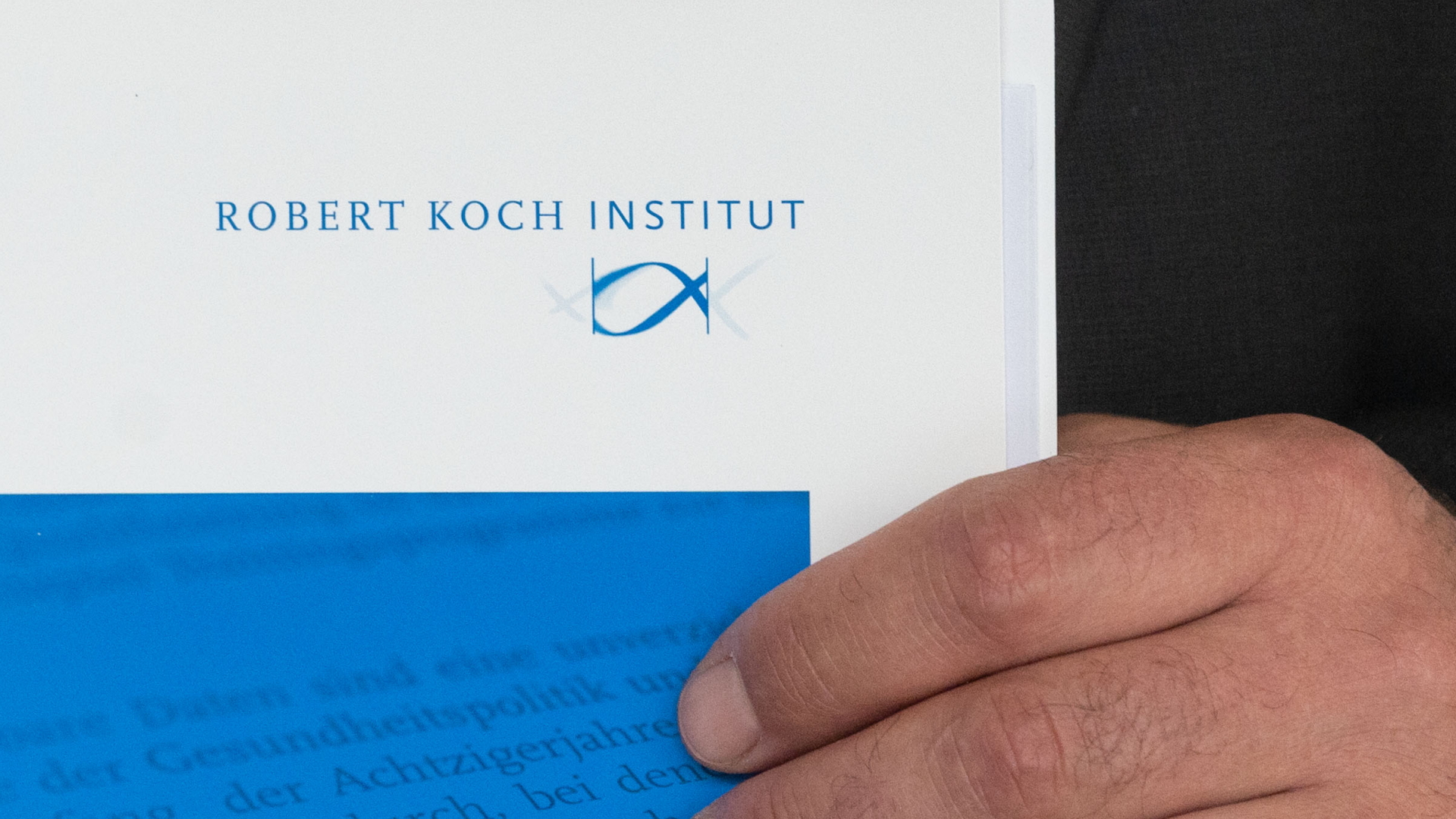 Eine Hand hält eine Mappe mit dem Logo des Robert-Koch-Instituts.