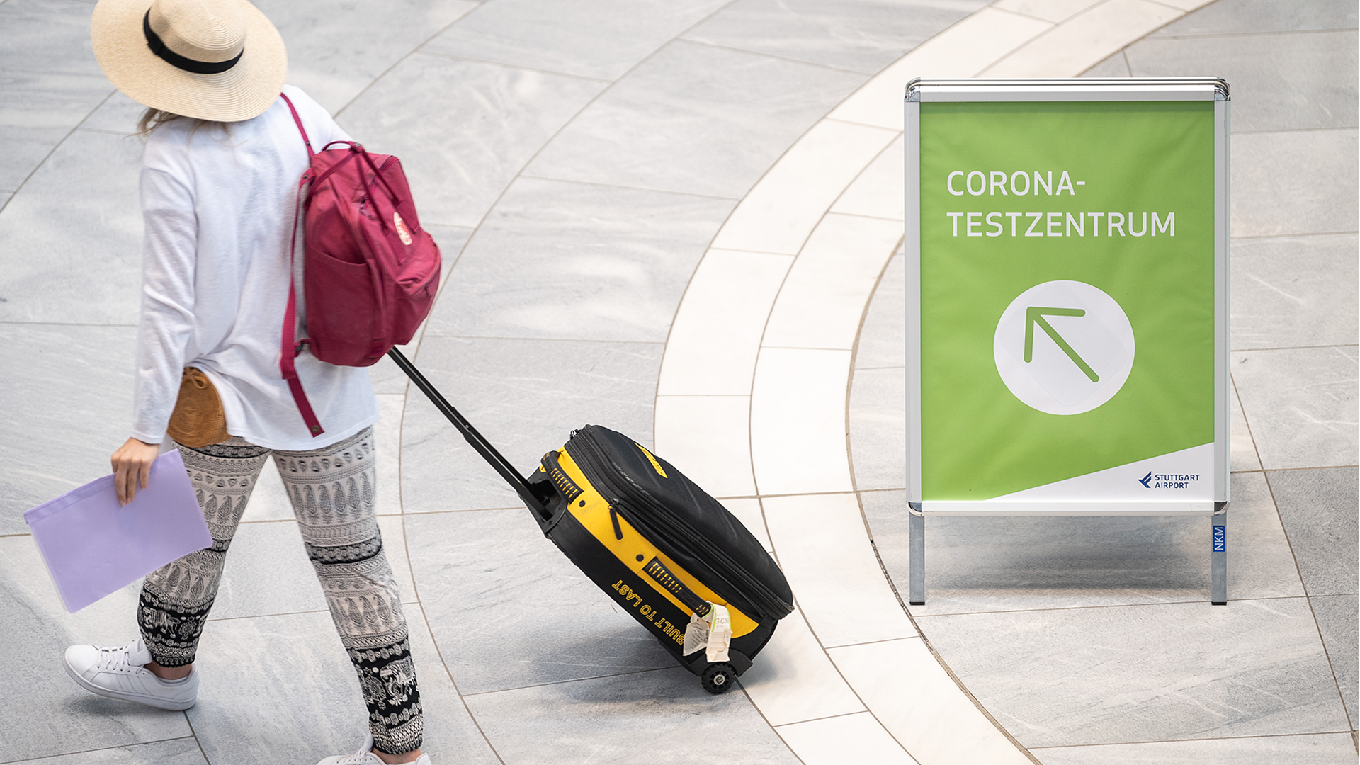 Eine Frau geht an einem Schild am Stuttgarter Flughafen vorbei, auf dem "Corona-Testzentrum" steht.