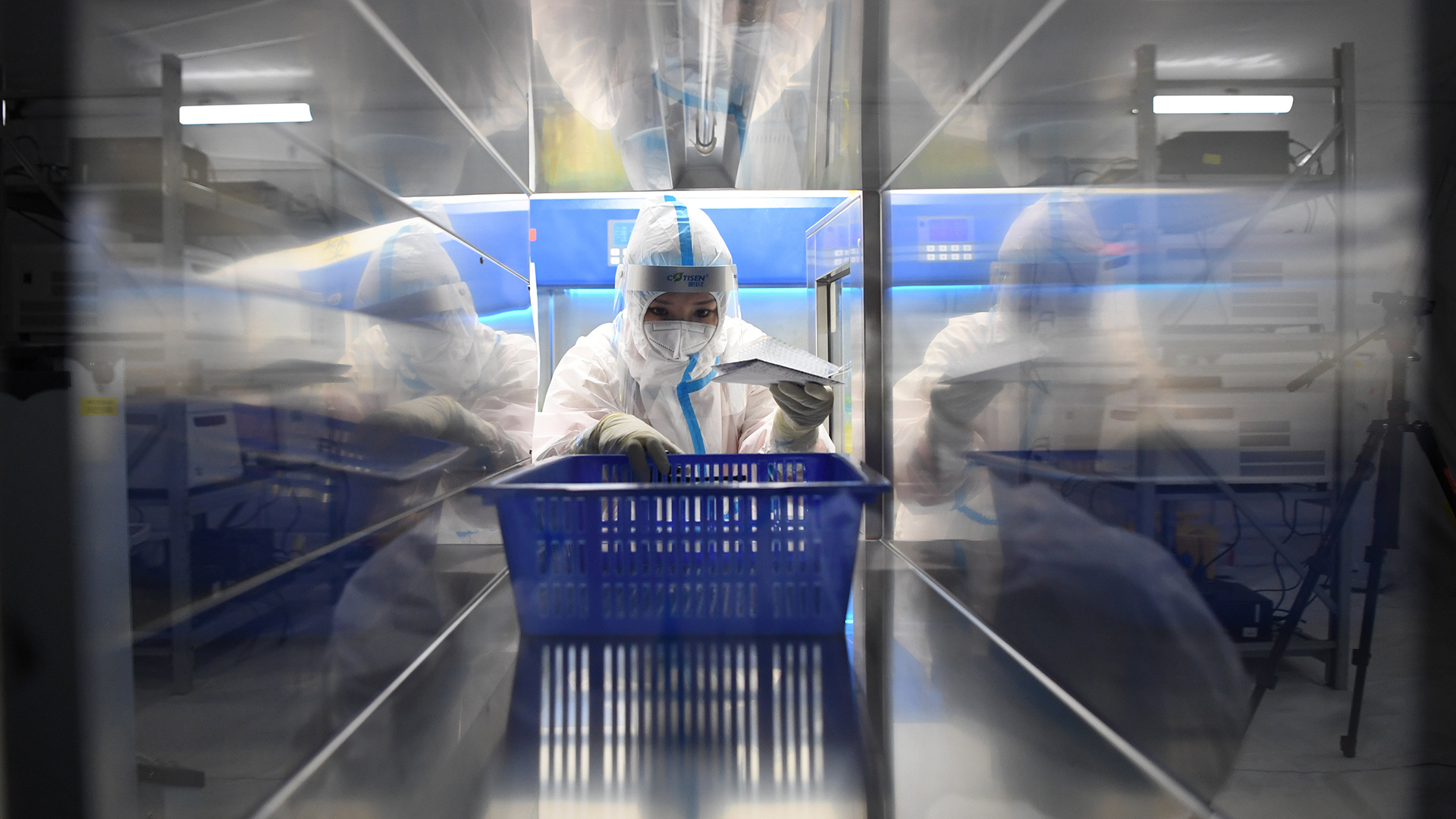  Eine medizinische Angestellte trägt einen Schutzanzug und hat einen blauen Korb in der Hand, während sie in einem chinesischen Testlabor für Corona-Tests arbeitet. | dpa
