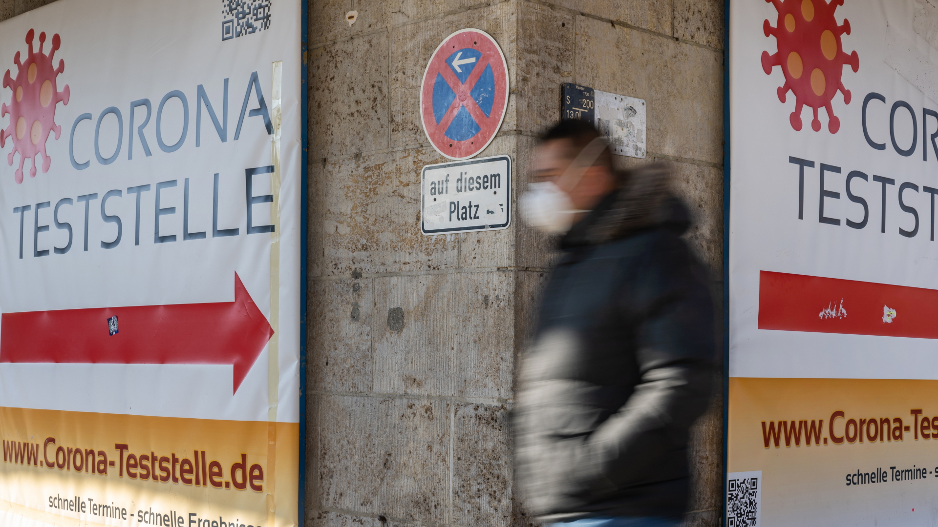Ein Mann geht in München (Bayern) an einem Plakat mit der Aufschrift "Corona-Teststelle" vorbei. | dpa