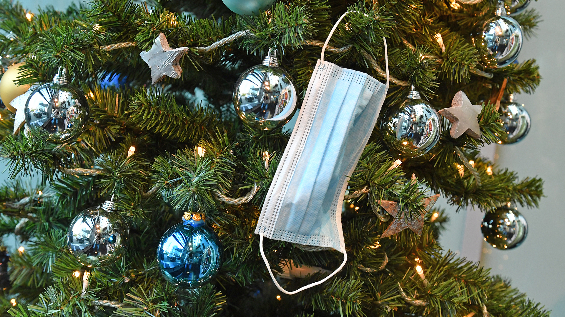 Ein Mundschutz hängt an einem weihnachtlich geschmückten Tannenbaum.