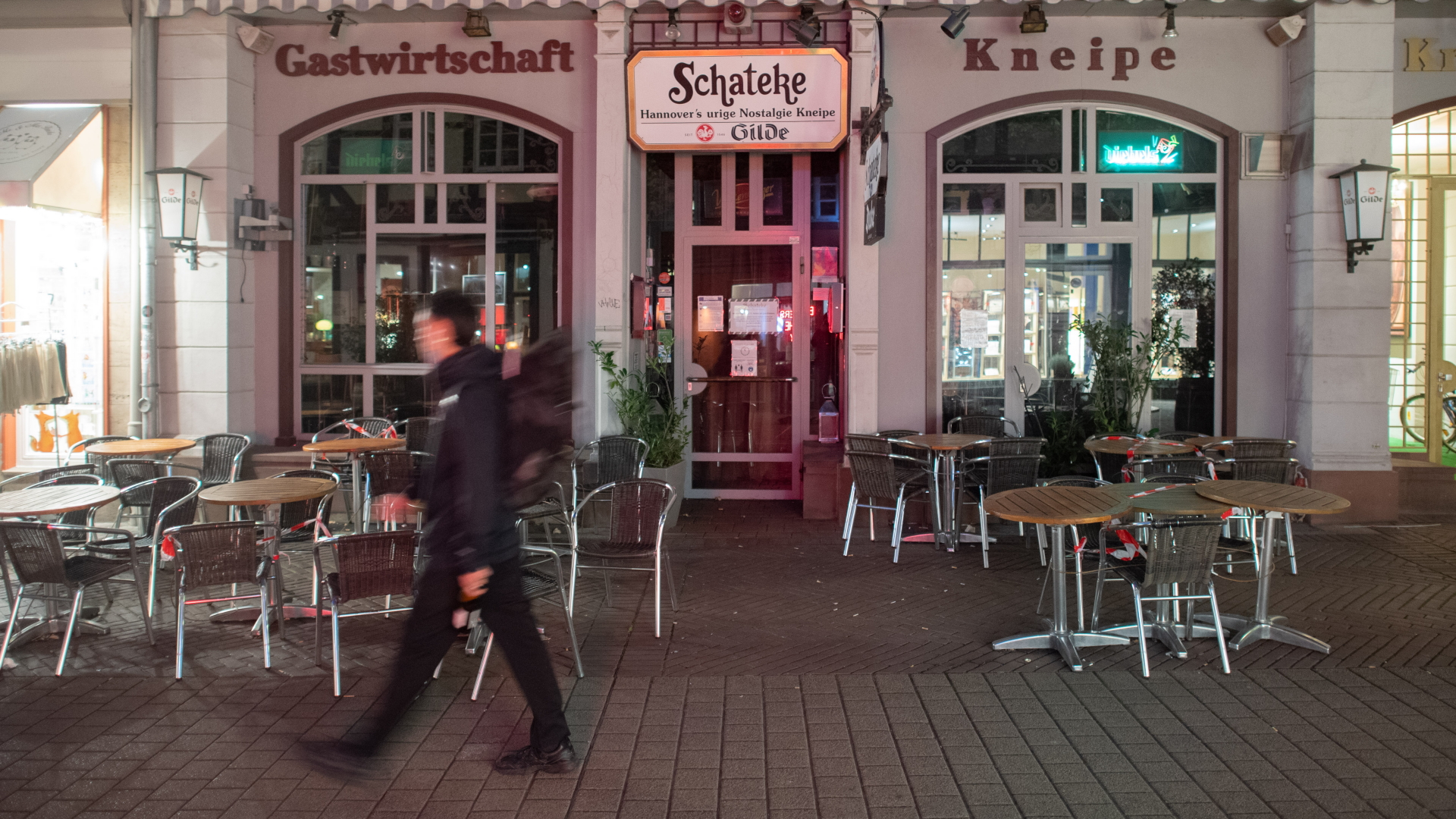 Ein Mann läuft abends in Hannover an einer geschlossenen Kneipe und Gaststätte vorbei.