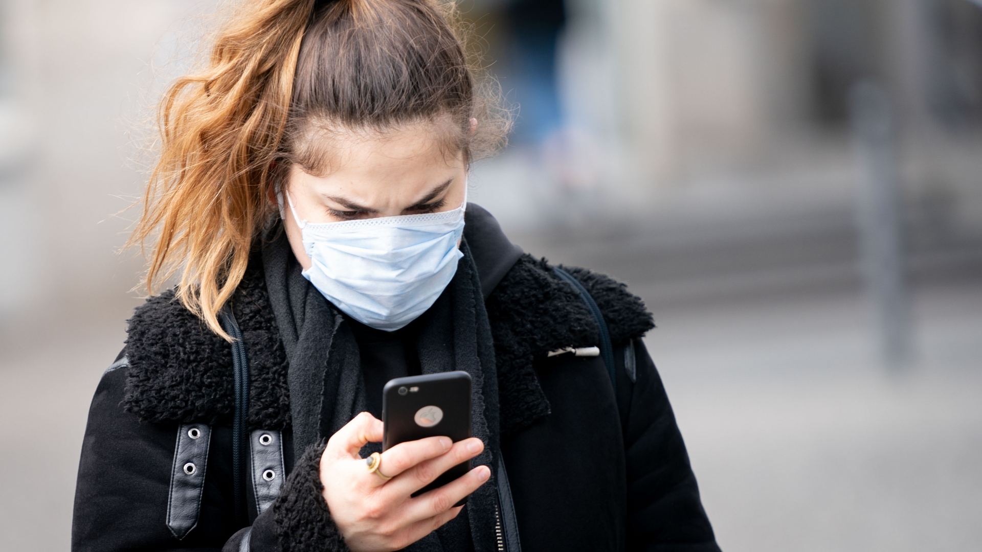 Eine Frau mit Schutzmaske gegen das Coronavirus blickt auf ihr Handy. | dpa