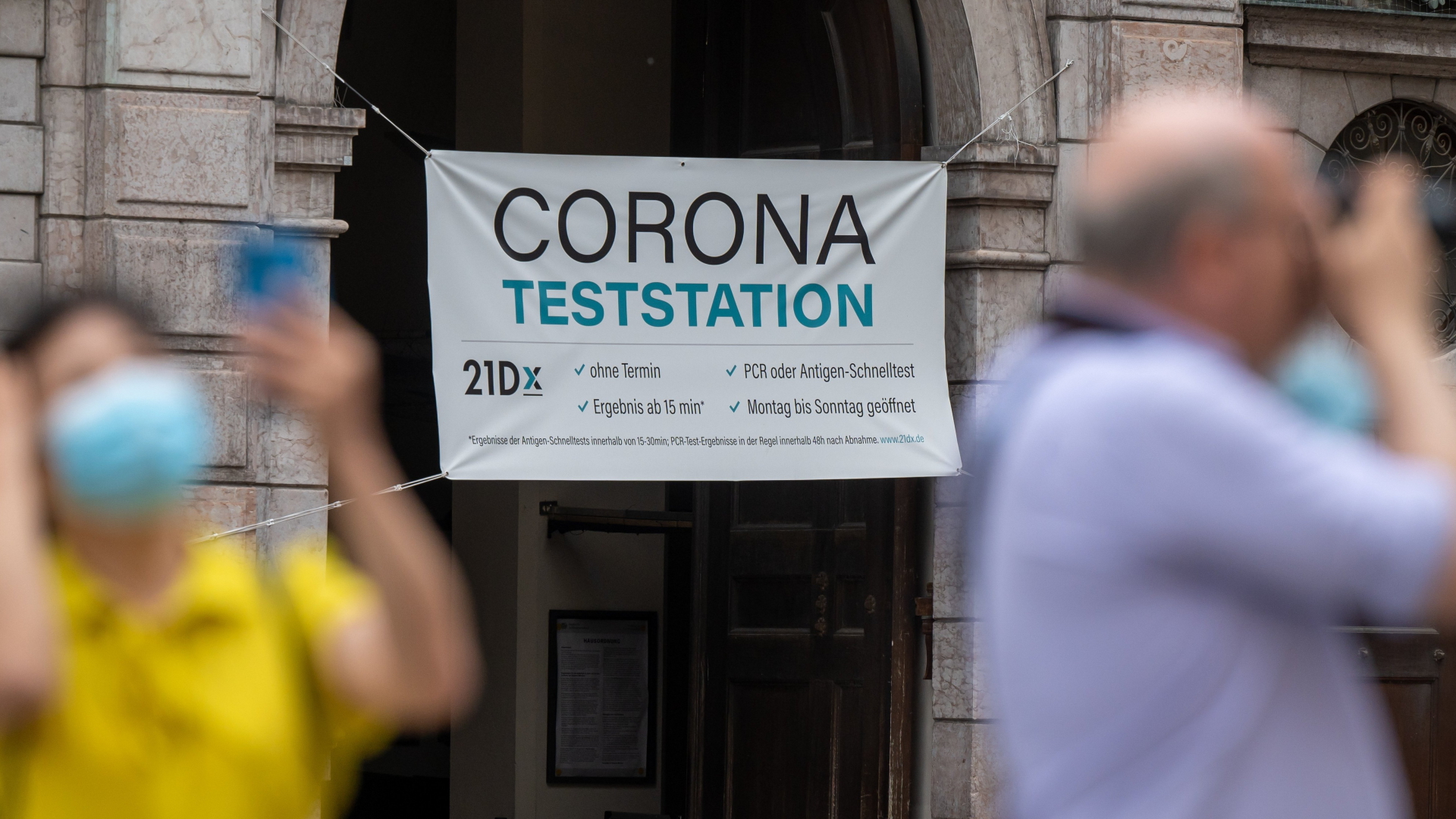 Passanten stehen in der Münchener Innenstadt vor einer Corona-Teststation und fotografieren (Archivbild). | dpa