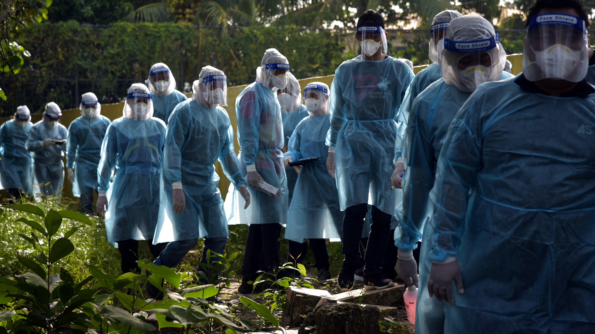 Helfer in Schutzkleidung laufen in einer Reihe durch Labuan in Malaysia. Sie versuchen, unter der Bevölkerung Corona-Infektionen zu erkennen. | dpa