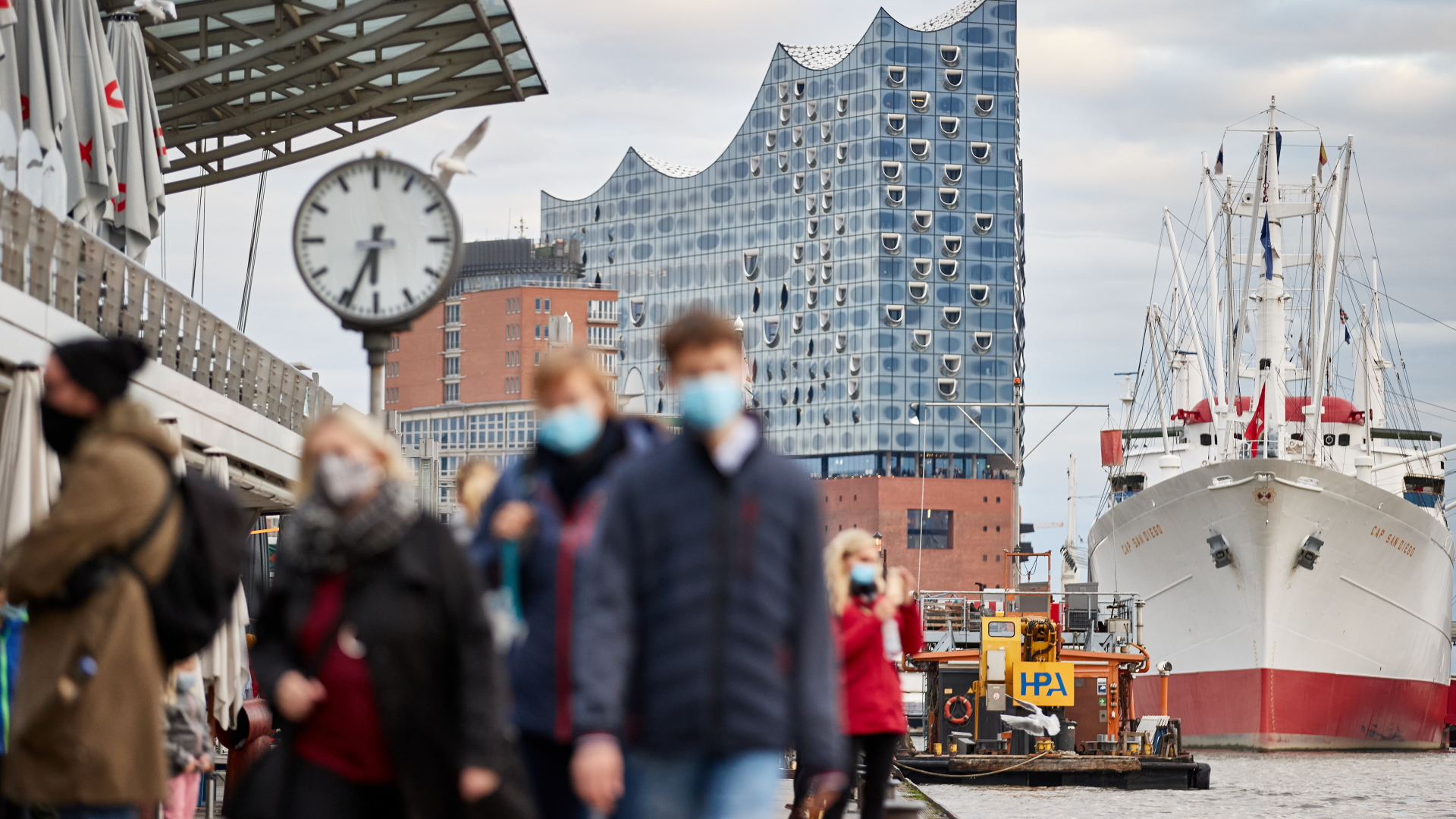 Fußgänger laufen mit Masken zum Schutz gegen das Coronavirus an den Landungsbrücken in Hamburg entlang.
