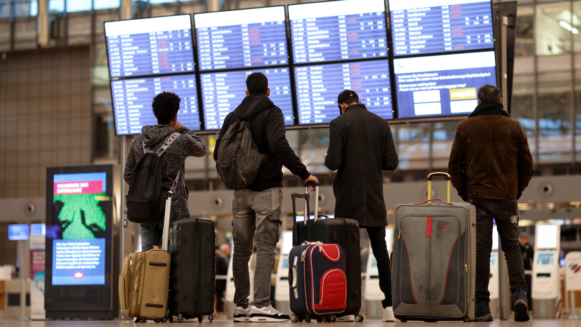 Reisende stehen am Hamburger Flughafen vor einer Anzeigetafel. | dpa