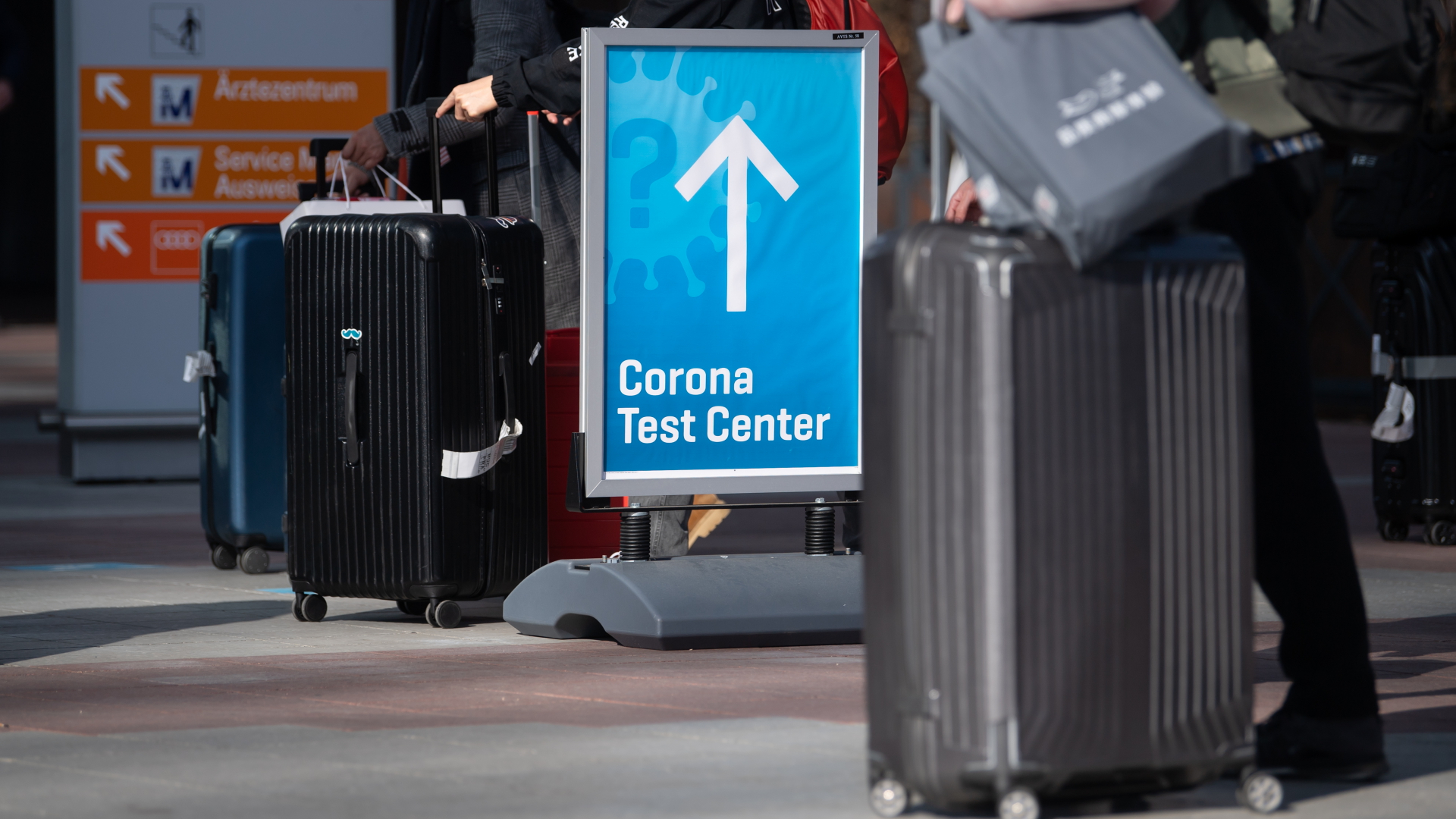 Reisende mit Koffern stehen vor einem Corona-Testzentrum auf dem Flughafen in München an. | dpa