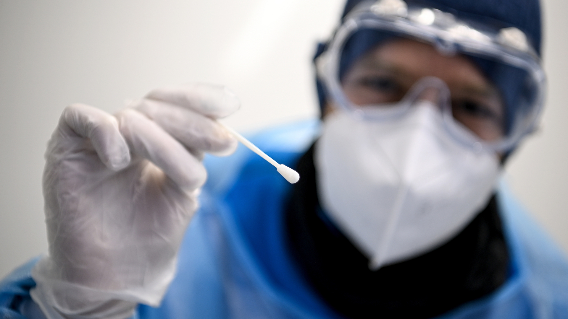 Ein Arzt in Schutzanzug hält ein Teststäbchen für die Entnahme einer Probe für einen PCR-Test in der Hand. | dpa