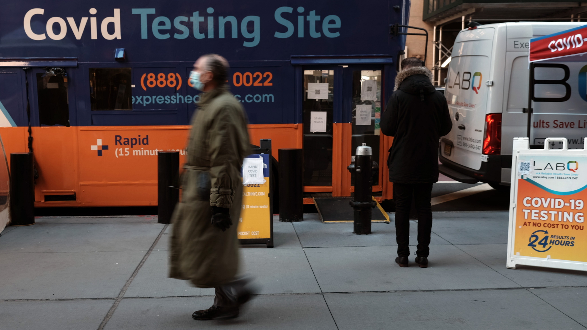 Menschen laufen in New York an einem Bus vorbei, der zu einer Corona-Teststation umgewandelt wurde. | AFP