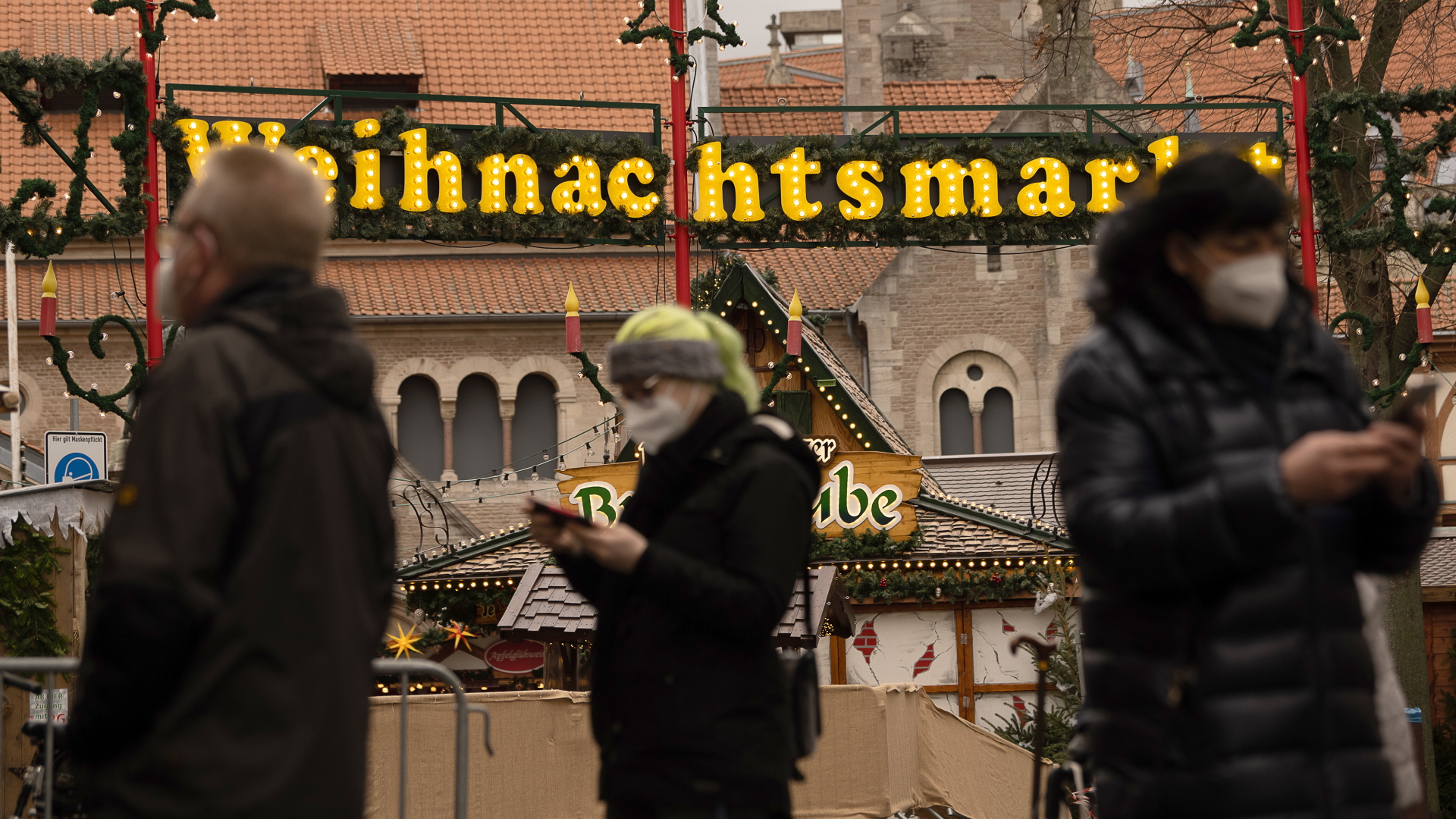 Passanten mit Schutzmaske laufen Anfang Dezember 2021 vor dem Weihnachtsmarkt in Braunschweig vorbei. | dpa
