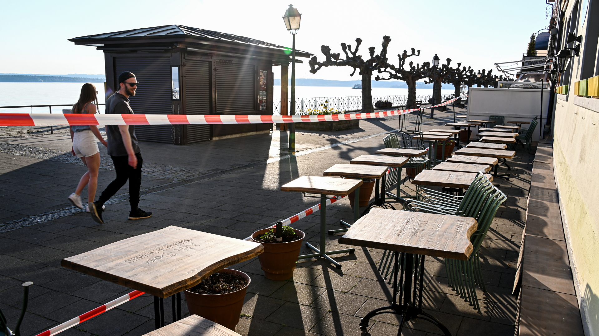 Ein junges Paar läuft bei strahlender Sonne an einem abgesperrten Restaurant vorbei. | dpa