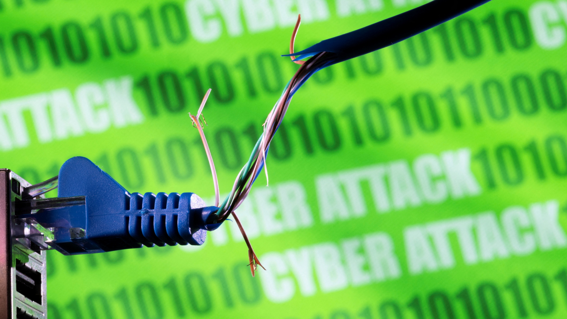 Ein defektes Netzwerkkabel vor einem Banner, auf dem das Wort Cyber Attack und ein binärer Code zu sehen sind.  | REUTERS