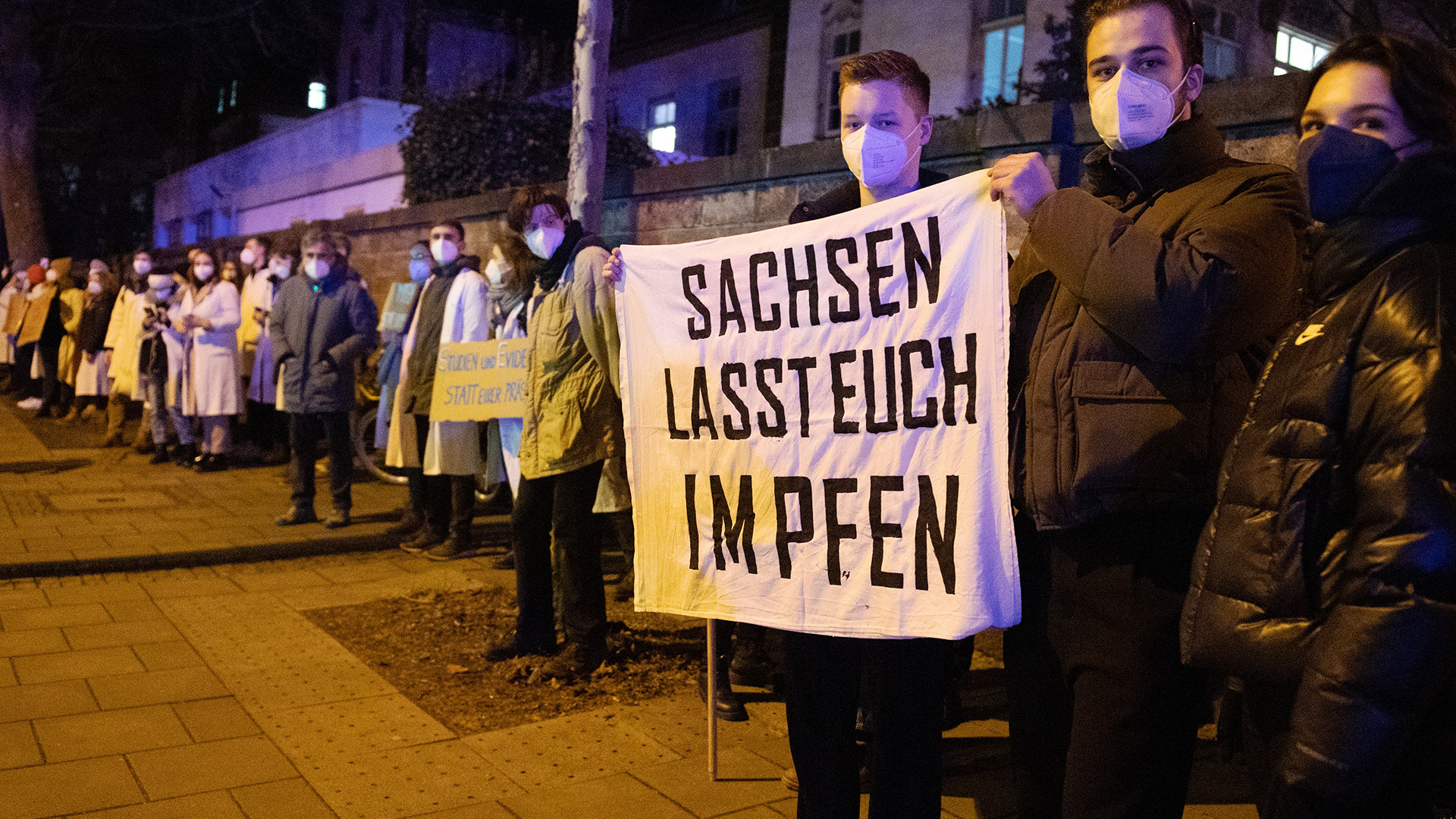 Gegendemonstranten halten anlässlich einer als «Spaziergang» deklarierten Demonstration von Impfgegnern und Kritikern der Corona-Maßnahmen vor dem Universitätsklinikum Dresden einen Banner. | dpa