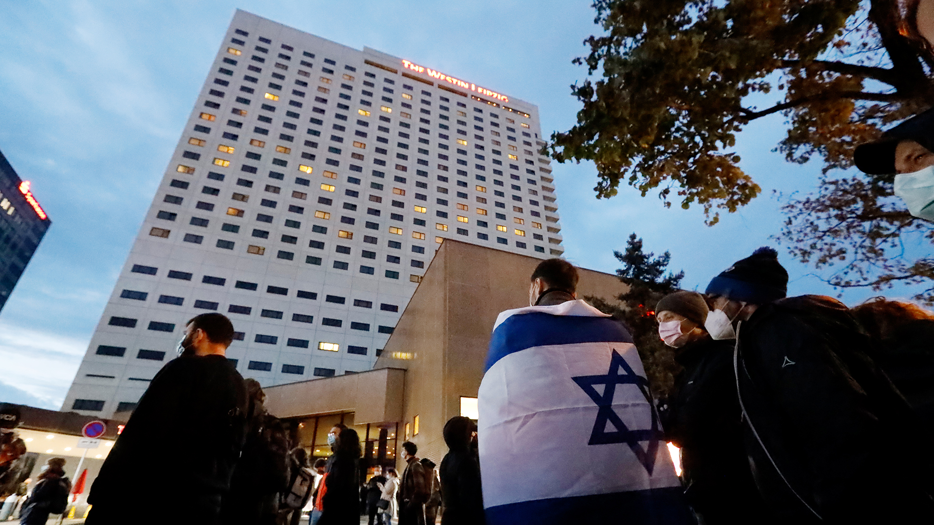 Ein Demonstrant trägt vor dem Hotel Westin in Leipzig die Fahne Israels über den Schultern. 