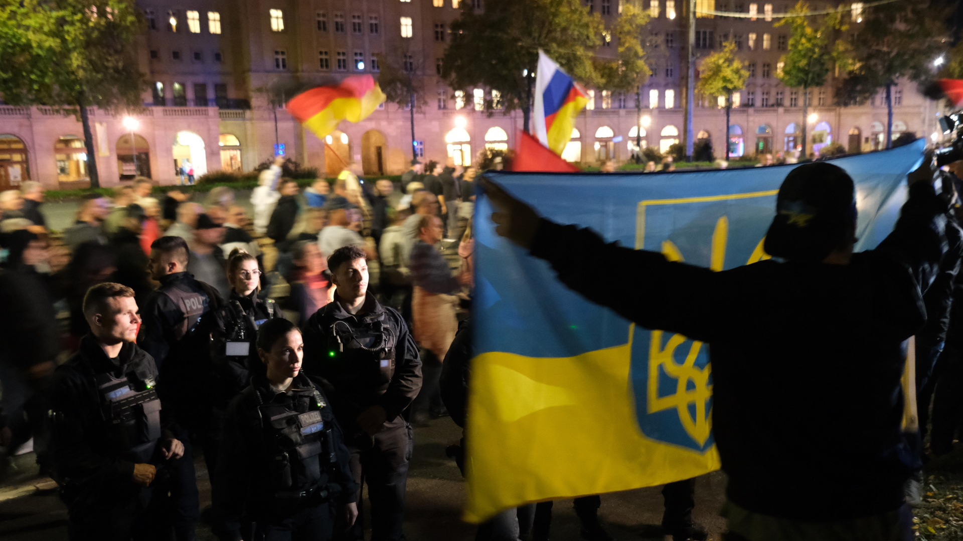 Teilnehmer einer Demonstration protestieren in Leipzig gegen die Russland-Politik der Bundesregierung, während ein Gegendemonstrant im Vordergrund eine ukrainische Fahne hält. | dpa
