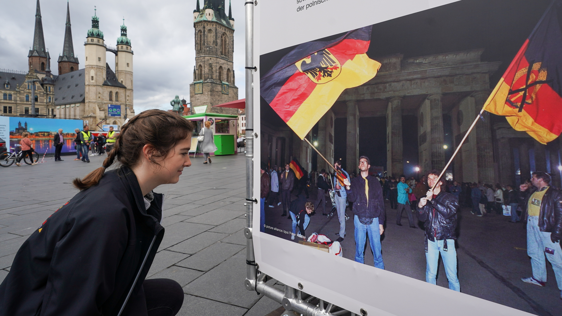 Eine junge Frau betrachtet ein Foto zum "Tag der Deutschen Einheit" in einer Ausstellung auf dem Marktplatz in Halle. | dpa
