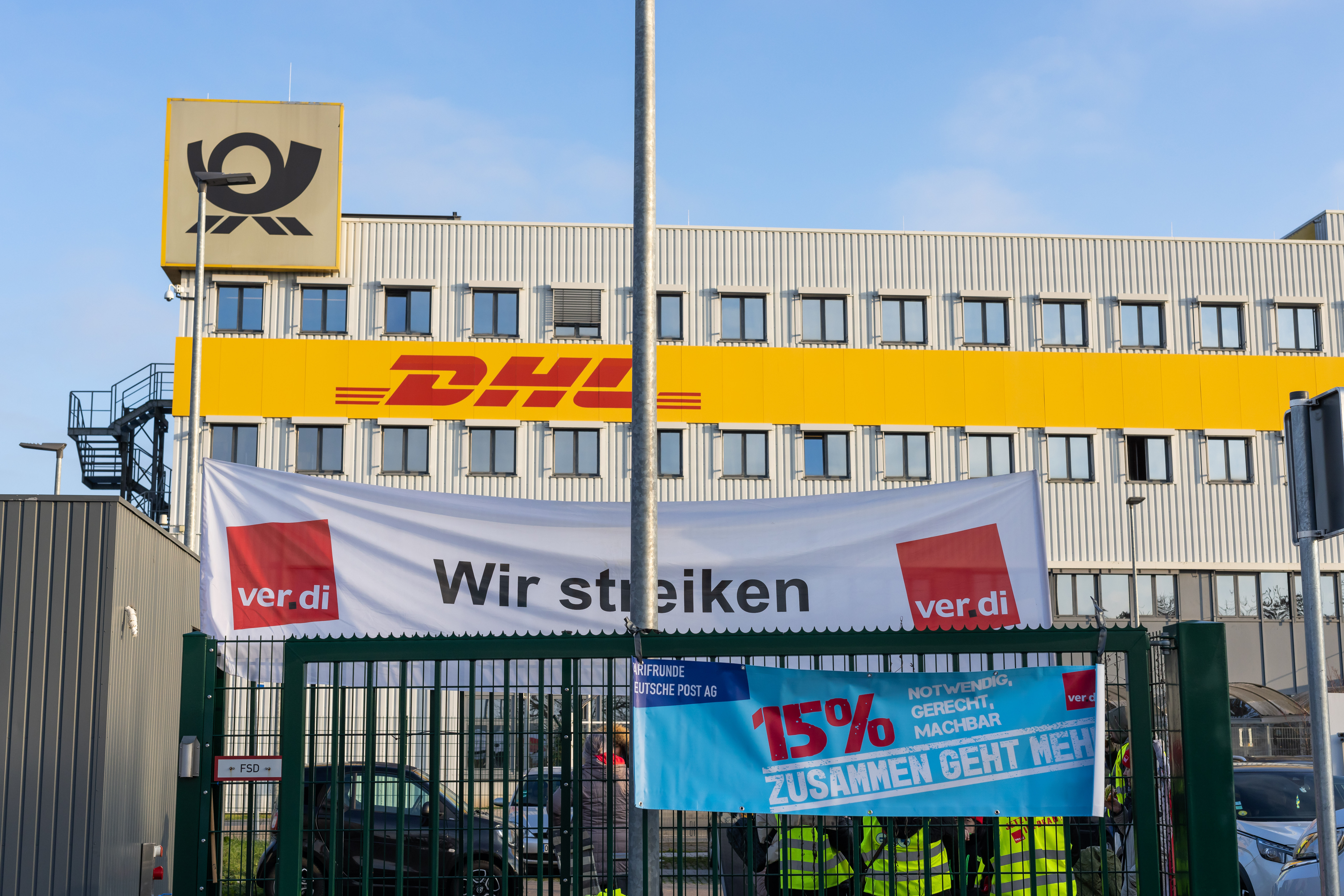 Ein Banner mit der Aufschrift "Wir streiken" der Gewerkschaft Ver.di hängt vor einem Gebäude des Paketdienstleisters DHL. 