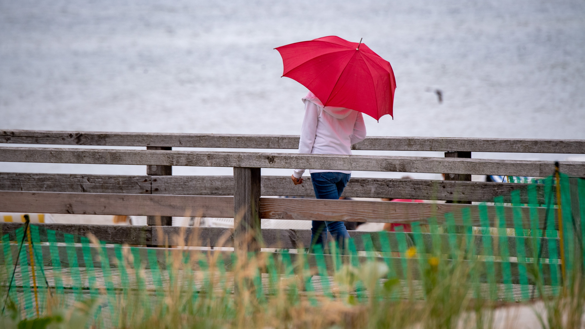 Eine Frau ist mit einem roten Regenschirm an der Ostseeküste auf der Seebrücke von Lubmin unterwegs | dpa