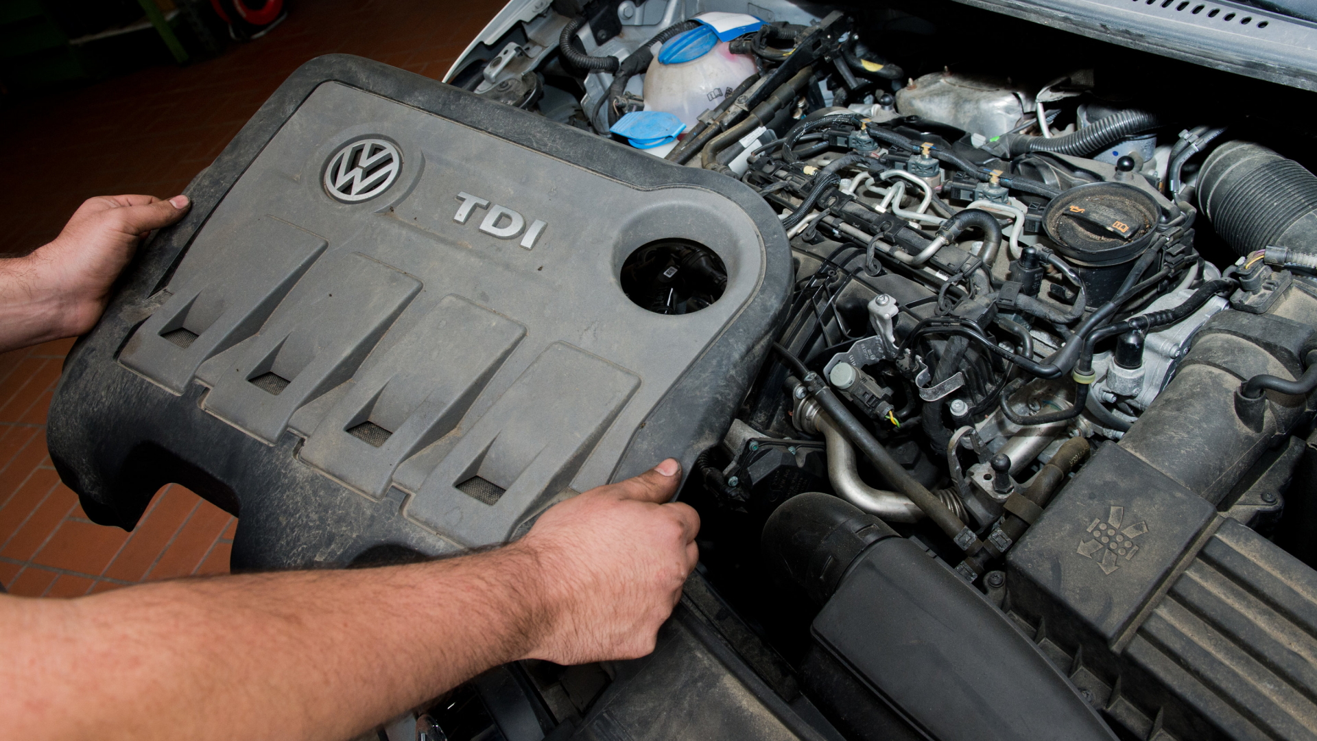 Ein KFZ-Techniker in einer Autowerkstatt hält die Abdeckung vor einem vom Abgasskandal betroffenen TDI-Dieselmotor. | dpa