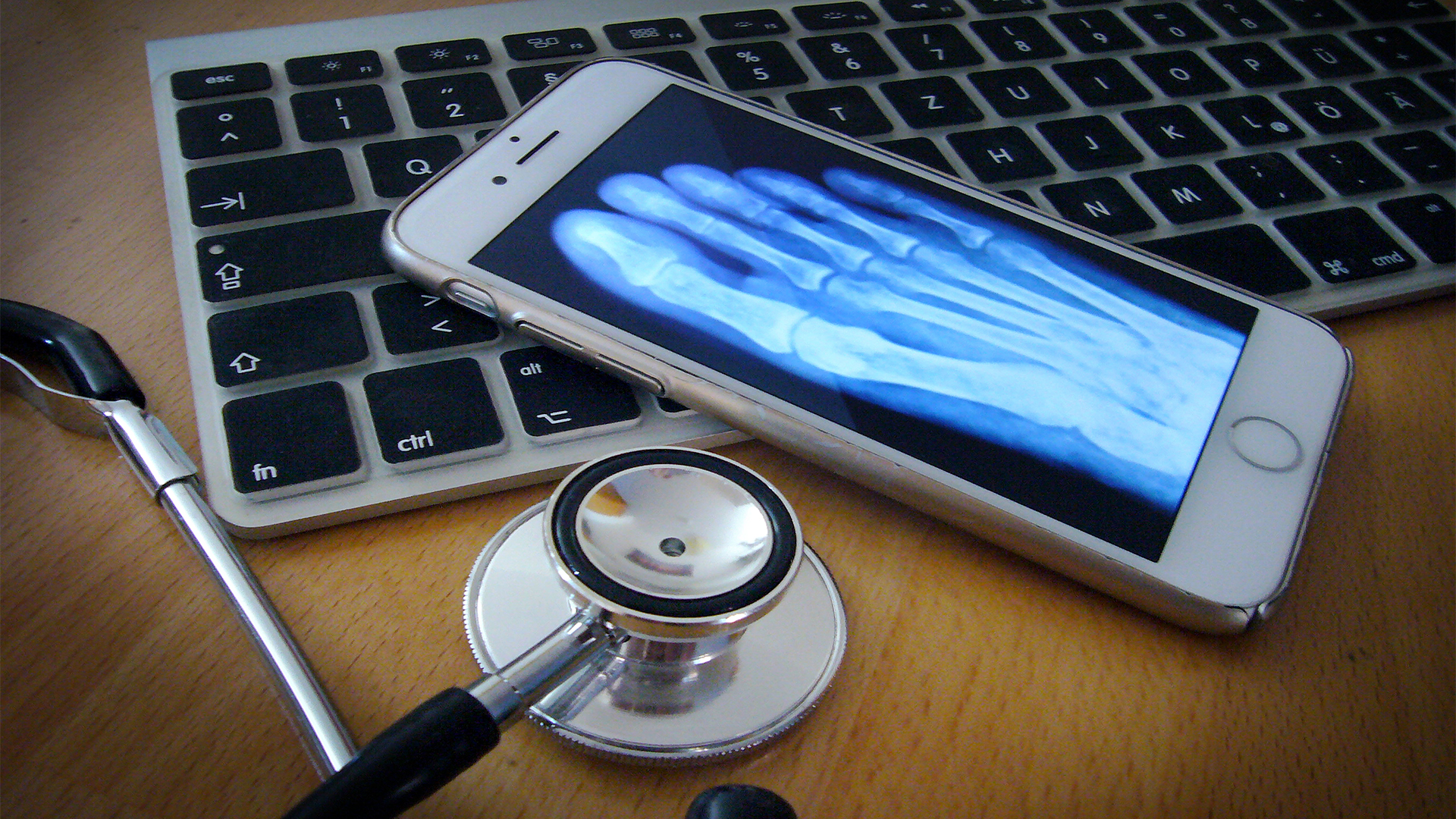 Ein Stethoskop liegt neben einem Handy und einer Tastatur.