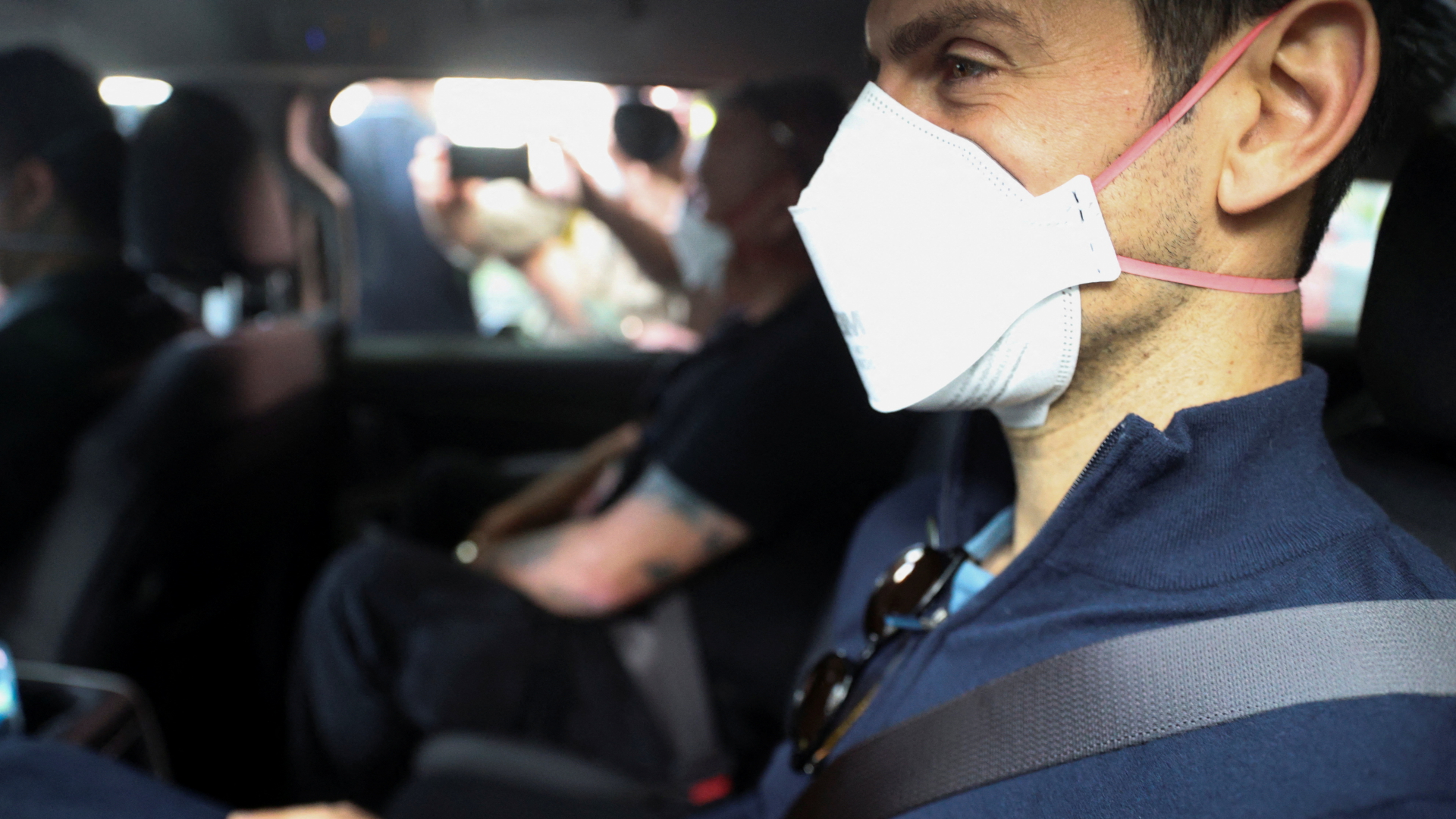 Novak Djokovic sitzt mit Maske in einem Auto. | REUTERS