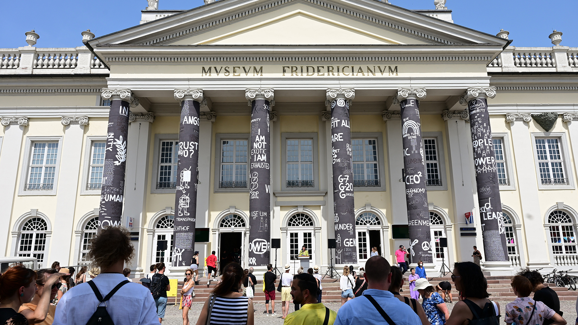 Besucher der documenta fifteen stehen vor dem Fridericianum, dessen Säulen der rumänische Künstler Dan Perjovschi gestaltet hat. | dpa