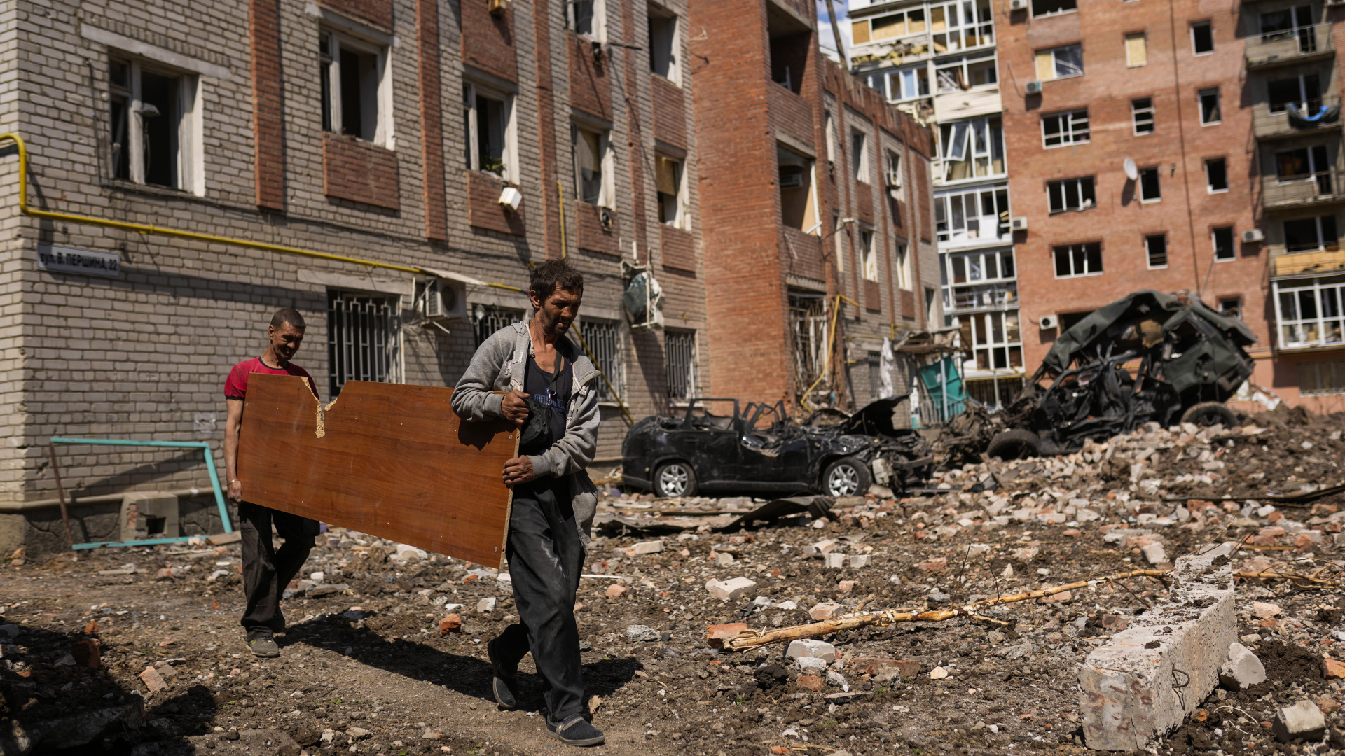 Zwei Menschen tragen eine Holzplatte durch einen zerbombten Wohnkomplex im Donbass. | dpa