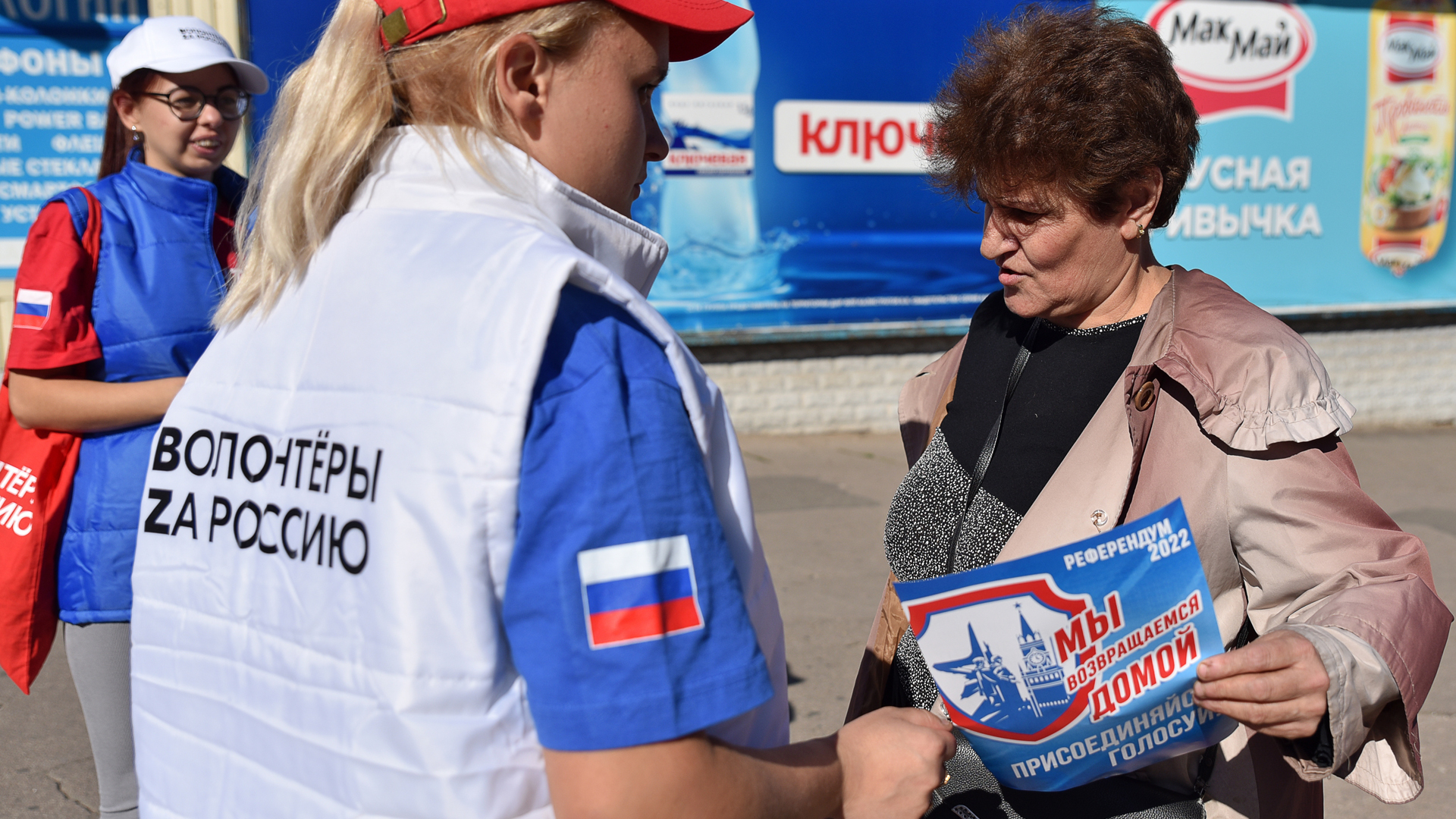Junge Frauen mit einer Weste der Aufschrift "Freiwillige für Russland" verteilen in Donezk Werbematerial für das Scheinreferendum an eine Frau. | picture alliance/dpa/TASS