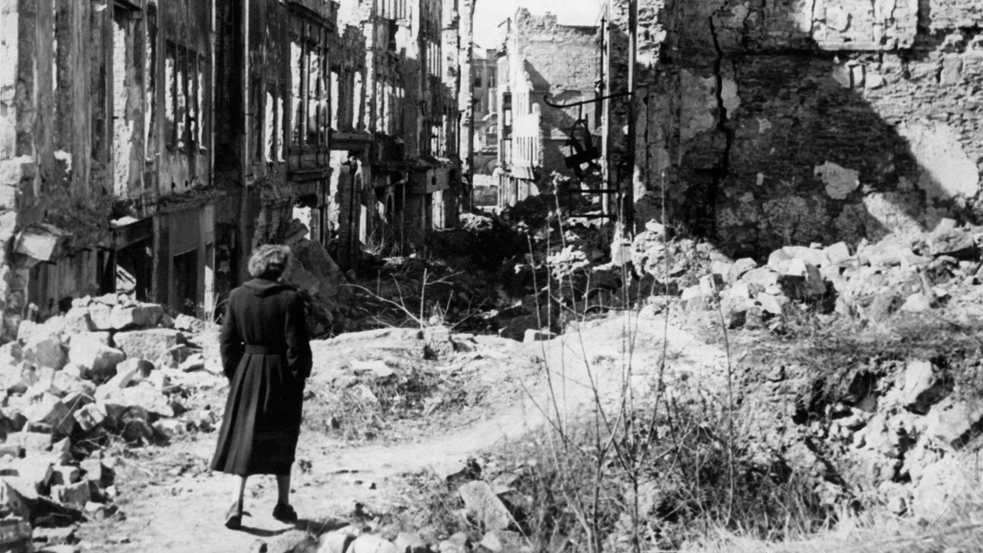 Eine Frau geht in einer Straße in Dresden an Häusern vorbei, von denen nach dem Zweiten Weltkrieg nur noch Ruinen geblieben sind | dpa