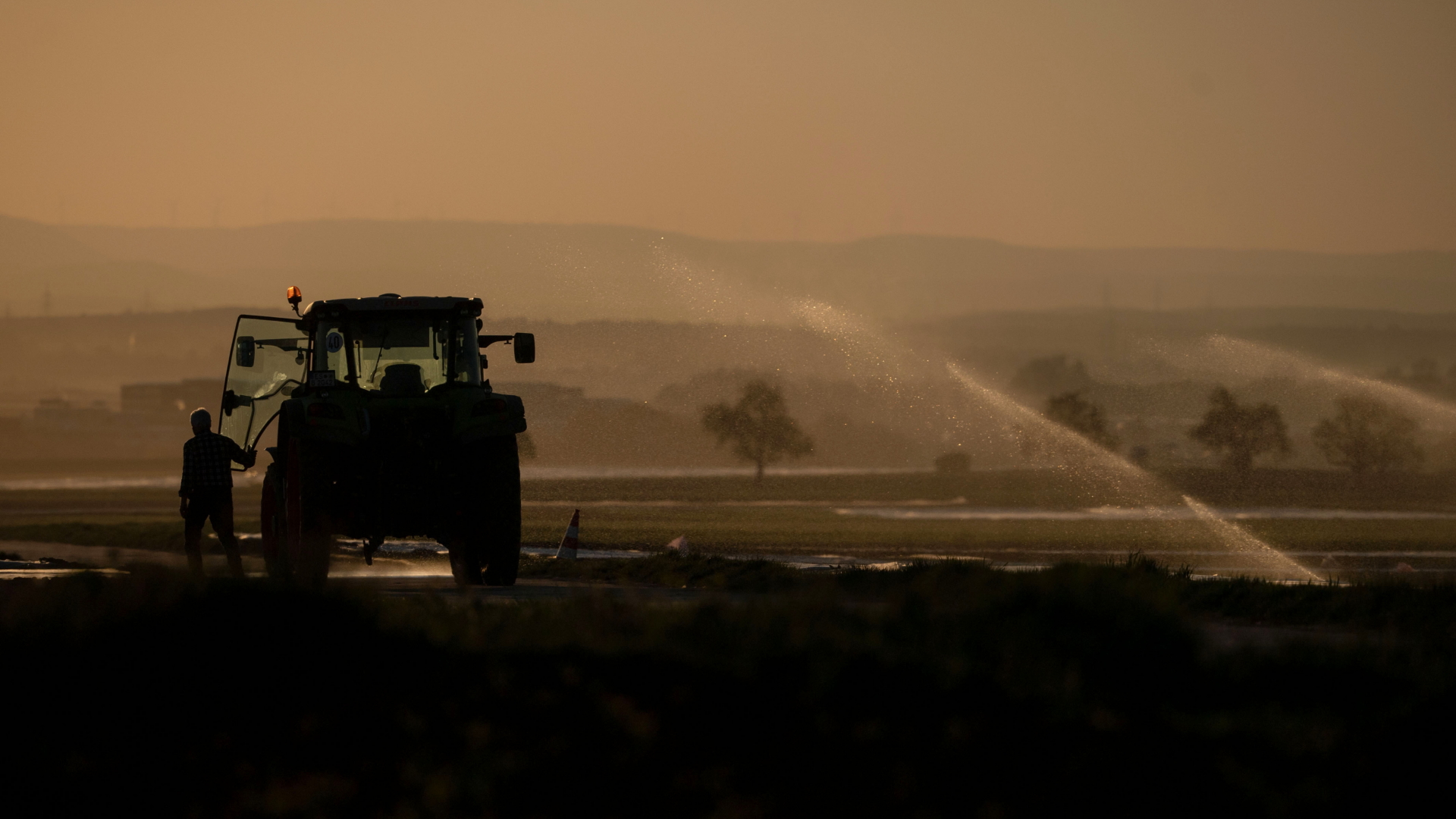 Ein Landwirt steht auf einem Feld, das bewässert wird.  | dpa