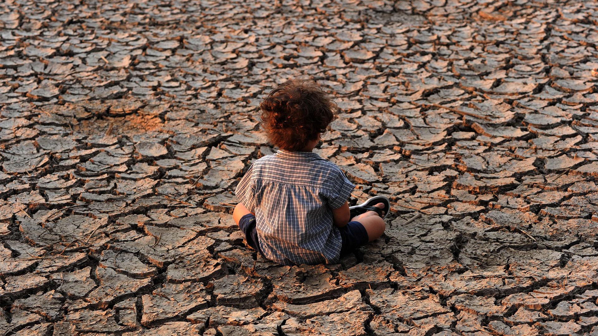 Ein Kind sitzt auf vertrocknetem Boden. | AFP