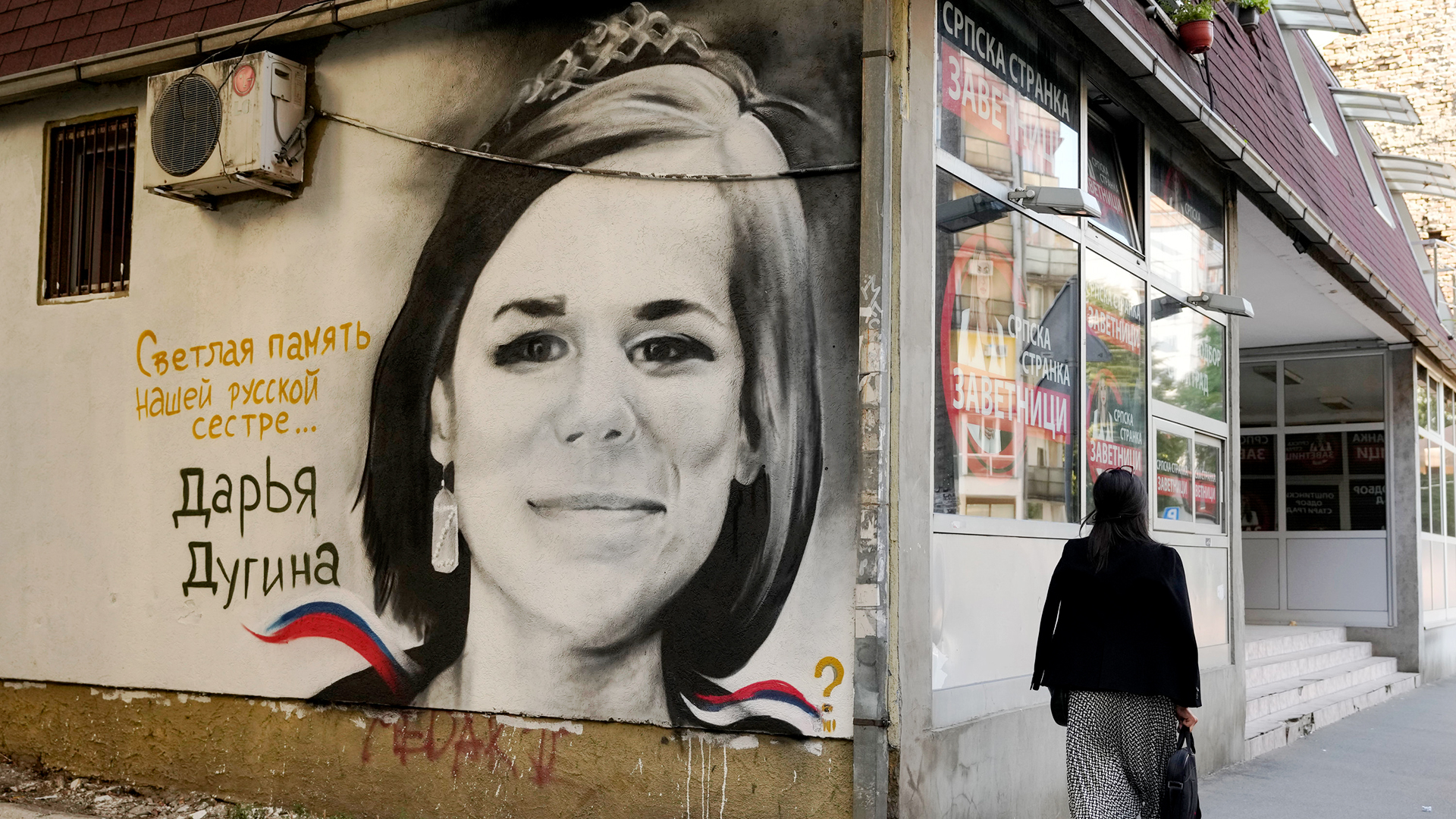 Eine Frau geht in Belgrad, Serbien, an einem Wandgemälde vorbei, auf dem Daria Dugina, die Tochter des Philosophen Alexander Dugin, abgebildet ist und das den Schriftzug "Helle Erinnerung an unsere russische Schwester" trägt.