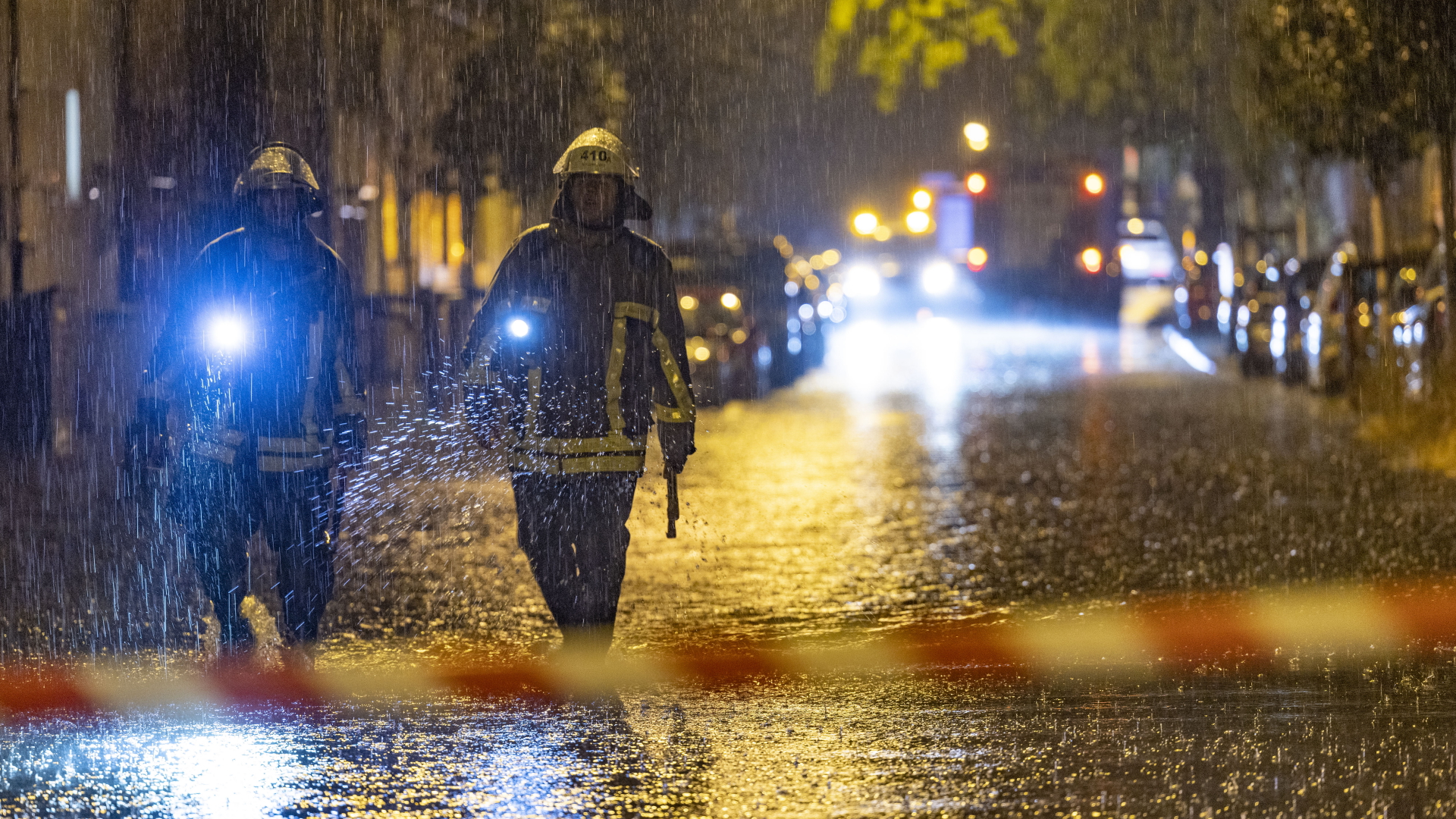 Feuerwehrleute suchen in einer Straße in Duisburg mit Taschenlampen nach Gullys
