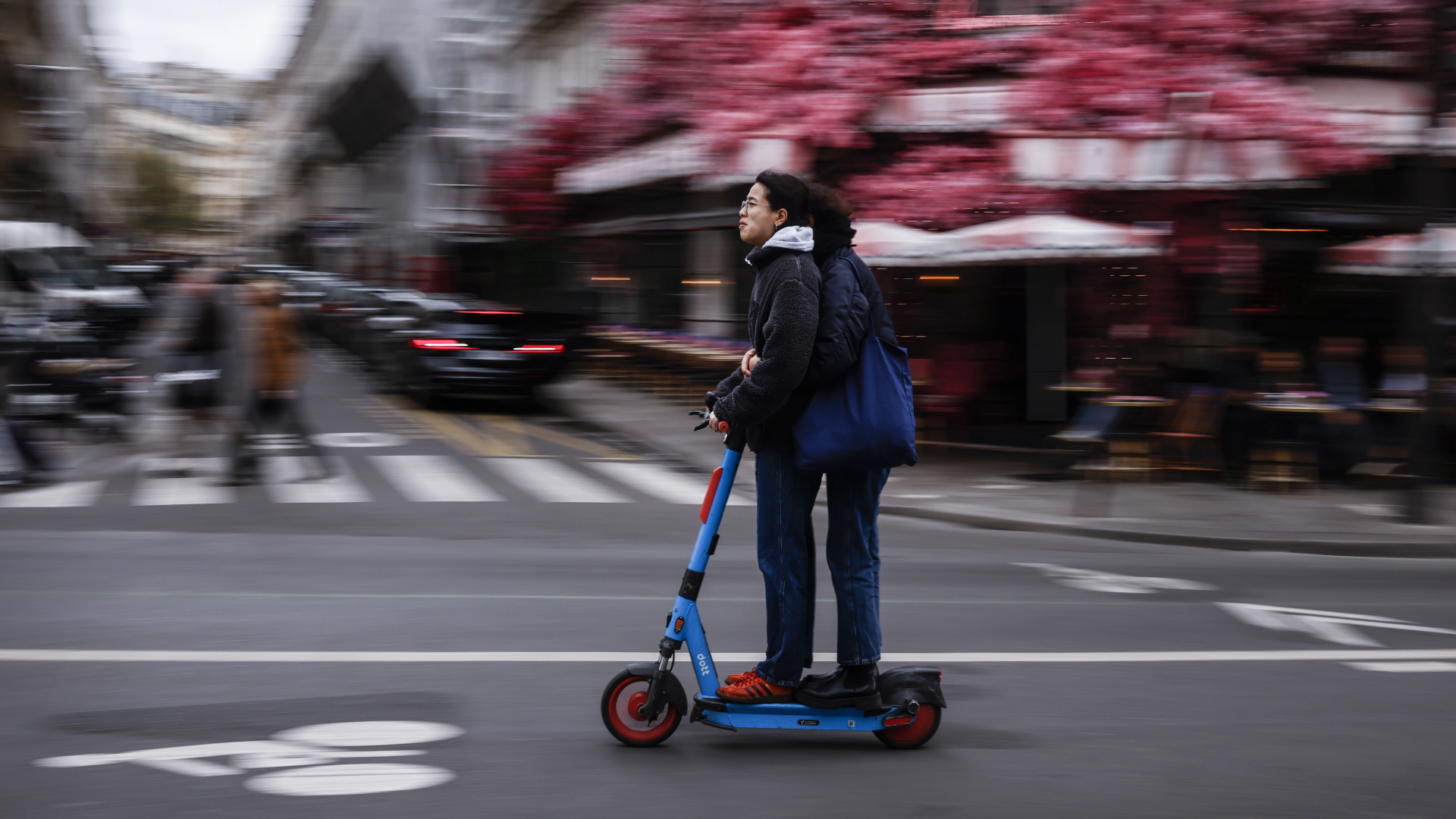 Zwei Menschen fahren auf einem Leihroller durch Paris.