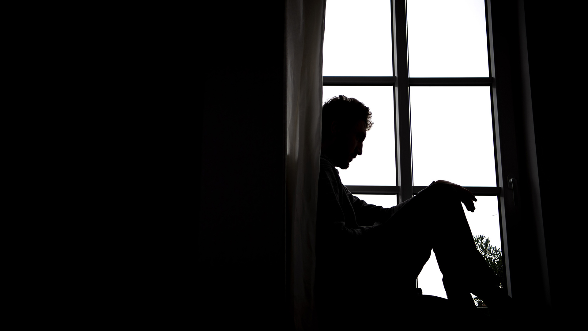 Ein Mann sitzt bei Dunkelheit vor einem Fenster. | picture alliance/dpa