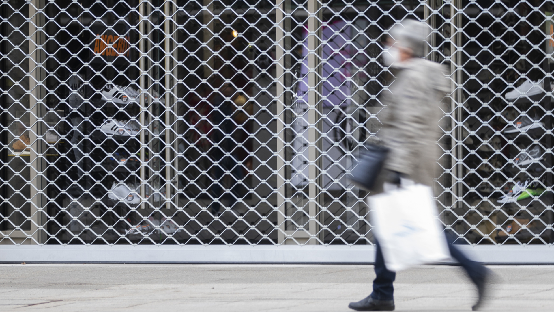 Eine Frau geht an einem mit einem Gitter verschlossenen Geschäft in Stuttgart vorbei. | dpa