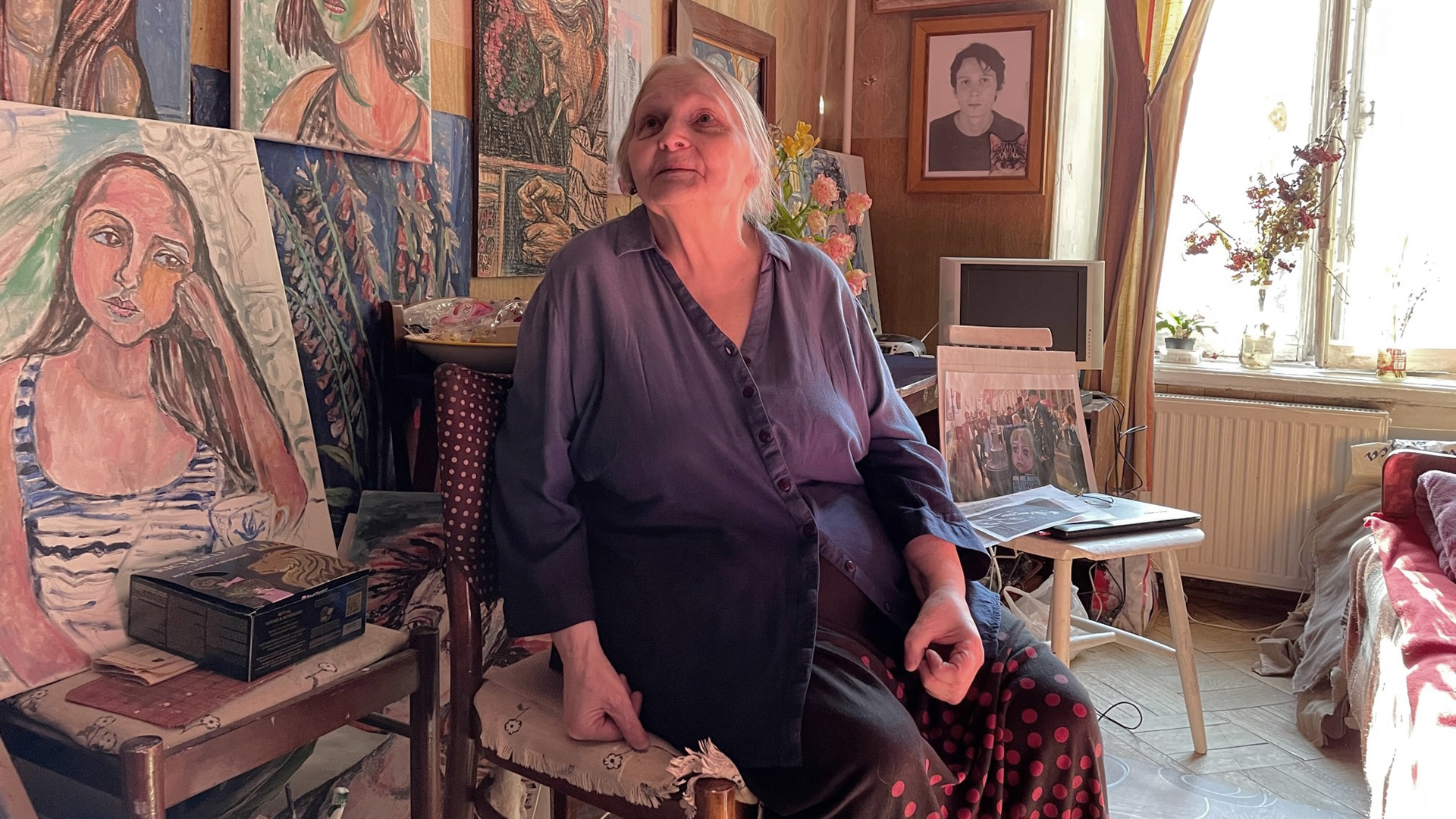 Die Malerin Elena Osipowa sitzt vor mehreren Bildern. | Martha Wilczynski/ARD-Studio Moskau