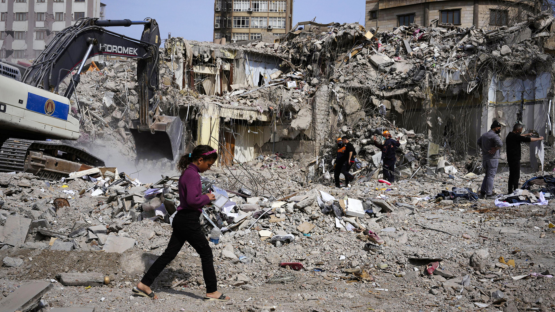Ein Mädchen geht durch das Trümmerfeld von Kahramanmaras, Türkei. Im Hintergrund Aufräumarbeiten. | picture alliance / Kyodo