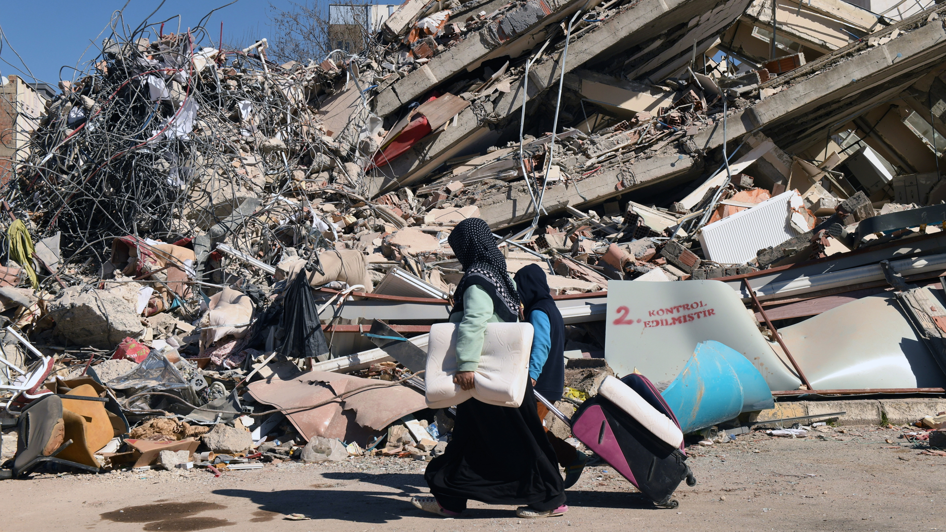 Menschen gehen in der türkischen Stadt Adiyaman an einem eingestürzten Gebäude vorbei. (Archivbild vom 18. Februar 2023) | dpa