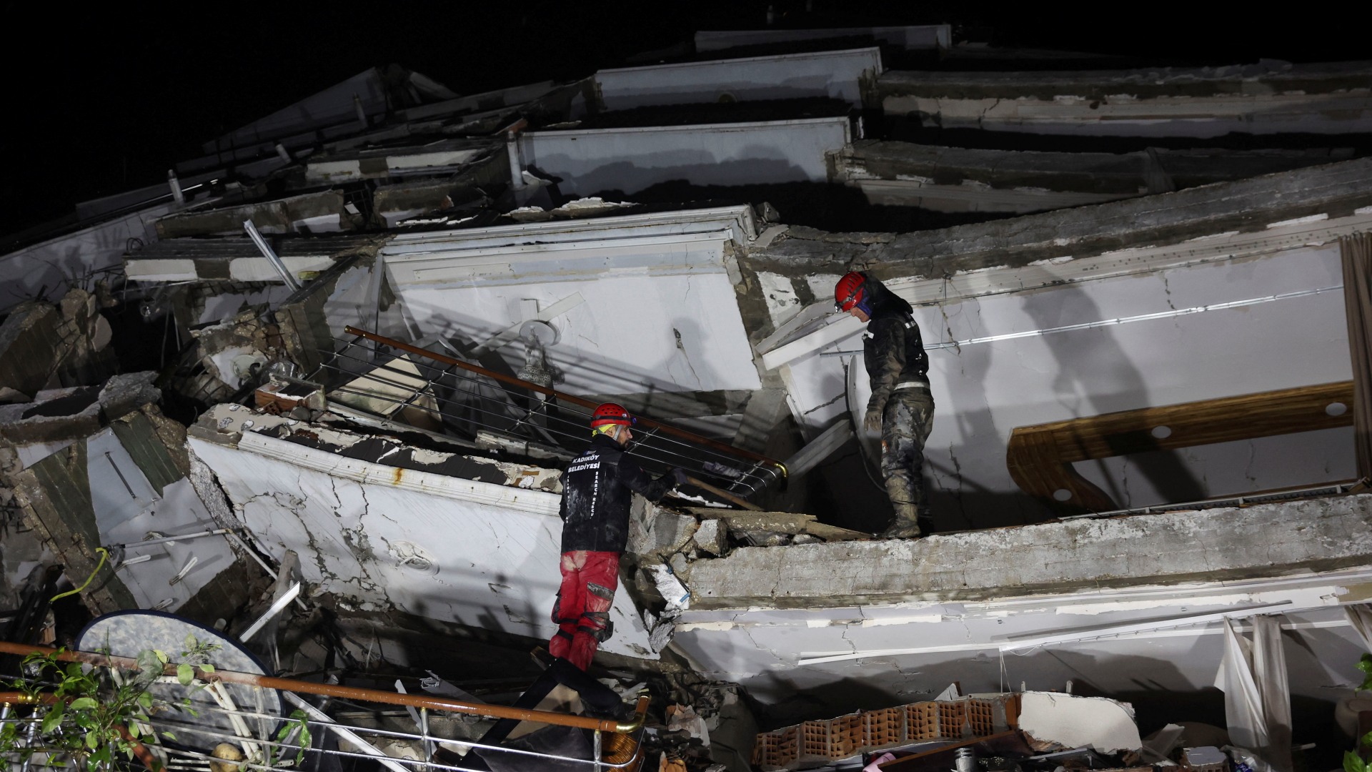 Zwei Rettungskräfte auf den Trümmern eines eingestürzten Hauses in der türkischen Stadt Antakya. | REUTERS