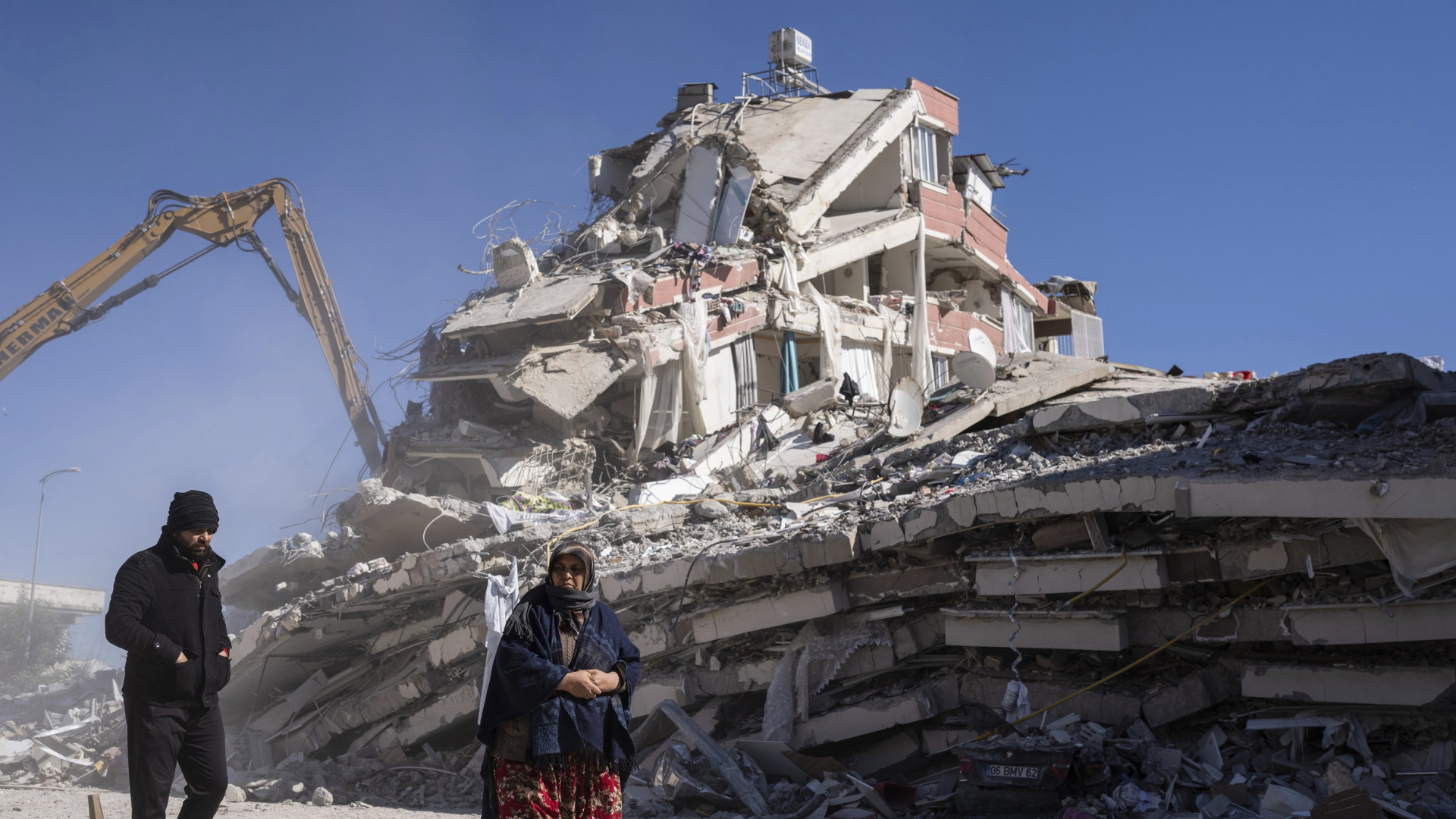 Ein eingestürztes Gebäude in der Türkei. Im Vordergrund laufen Menschen. | AP