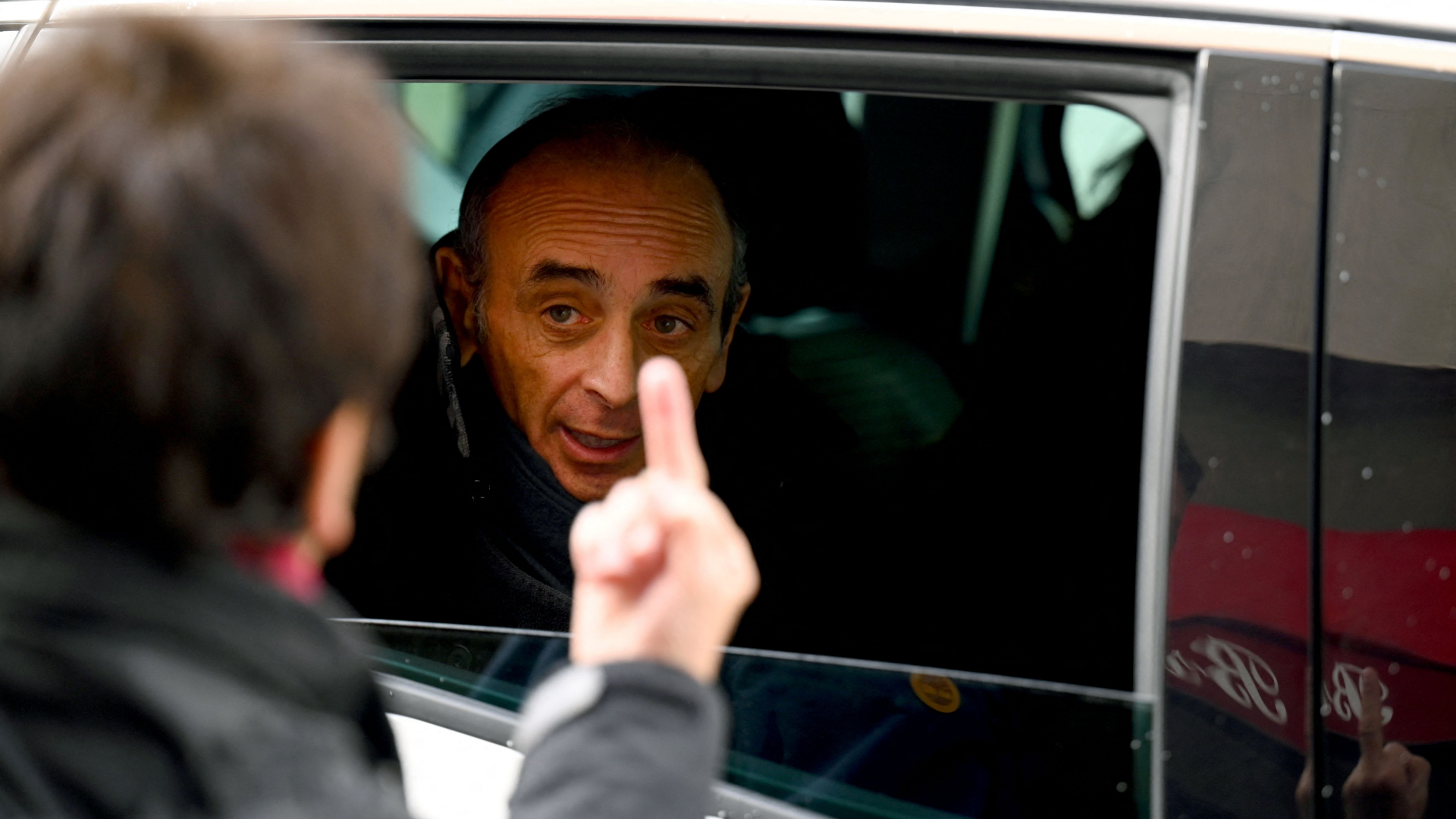 Eine Frau zeigt dem im Auto sitzenden Eric Zemmour den Mittelfinger. | AFP