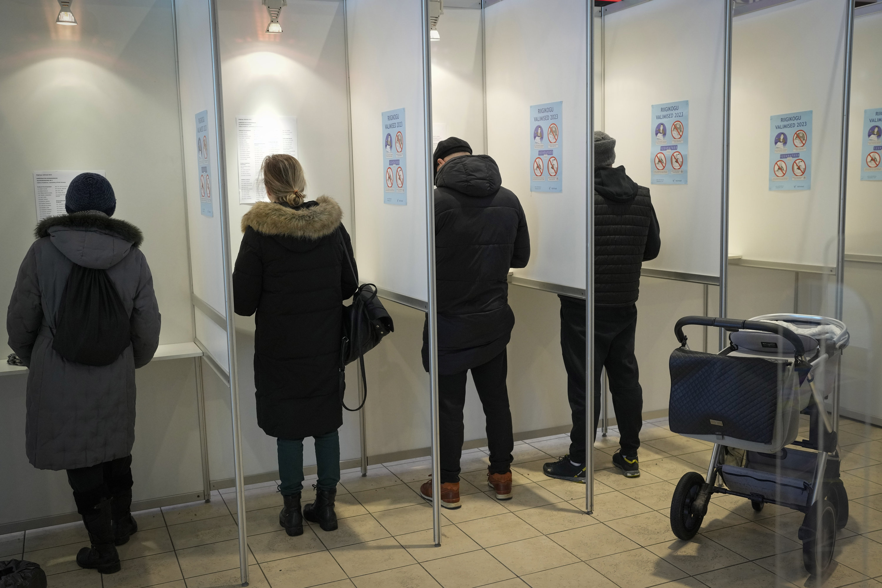 Vier Menschen, getrennt durch Zwischenwände, beim Abstimmen in einem Wahllokal in Tallinn, rechts am Rand parkt ein Kinderwagen | AP