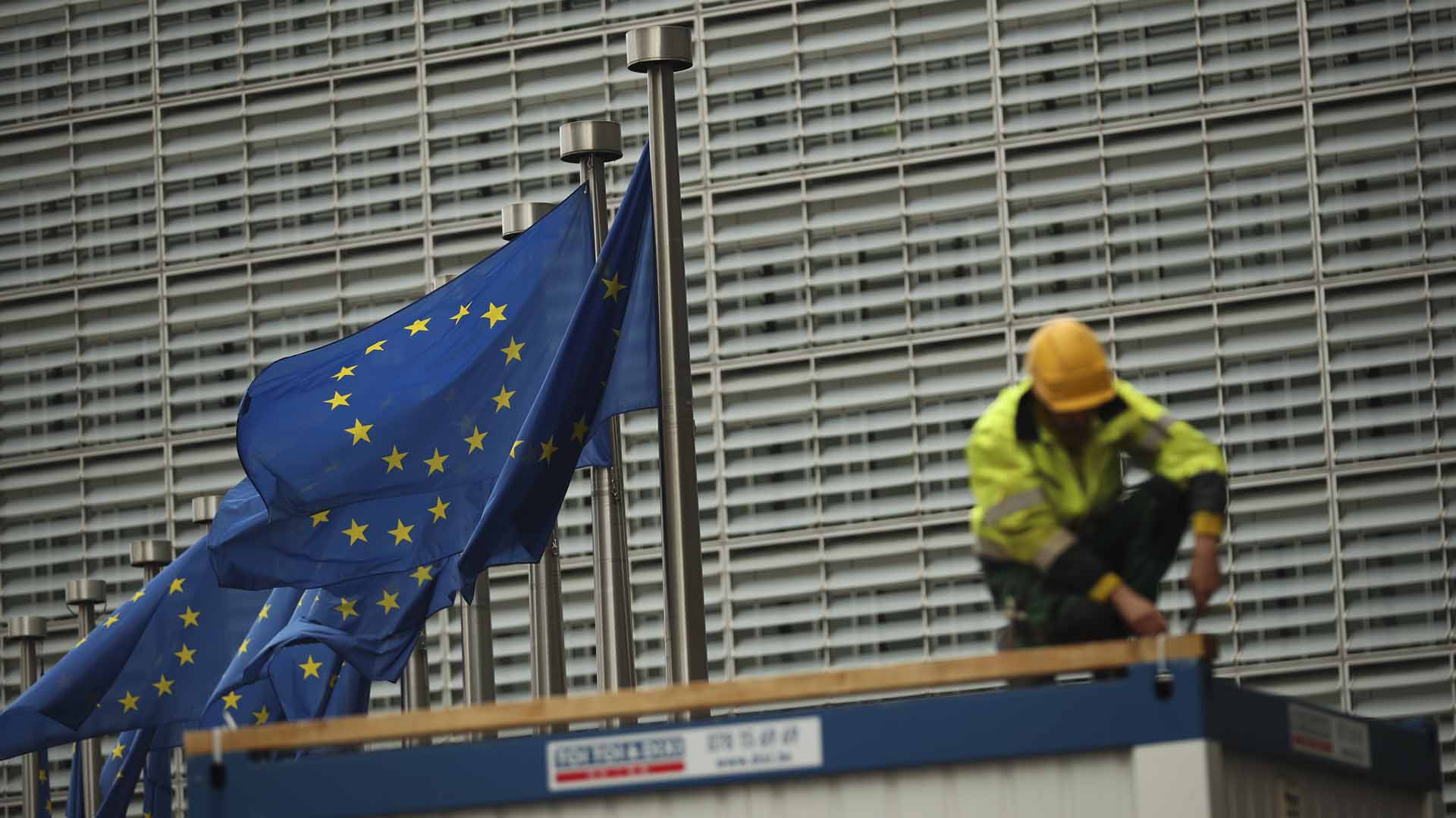 Ein Bauarbeiter arbeitet im Außenbereich des Hauptsitzes der EU-Kommission in Brüssel (Belgien), während neben ihm Europaflaggen wehen | picture alliance/dpa/AP