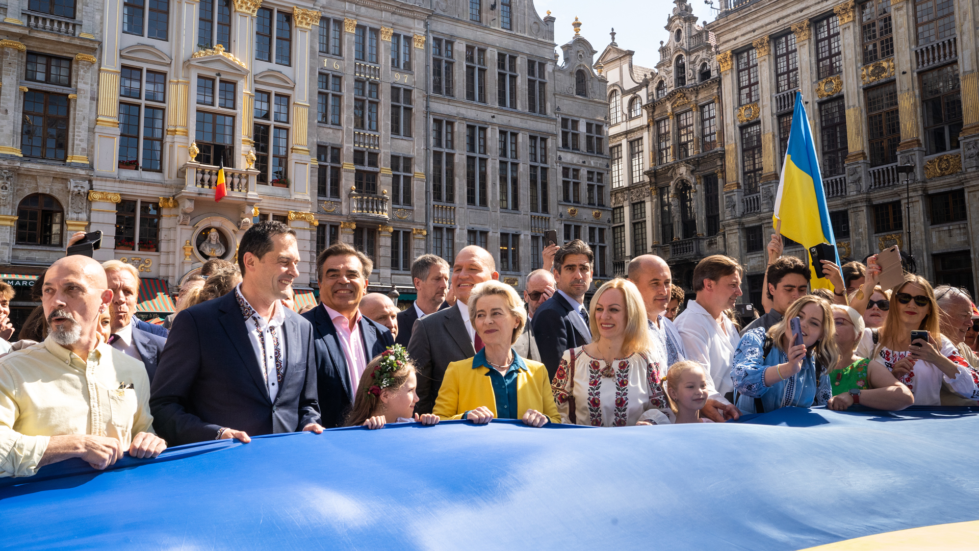 Brüssels Bürgermeister Philippe Close (2. von links) und EU-Kommissionspräsidentin Ursula von der Leyen halten bei einer Veranstaltung auf dem Grand Place - Grote Markt in Brüssel eine ukrainische Fahne. | picture alliance/dpa/BELGA